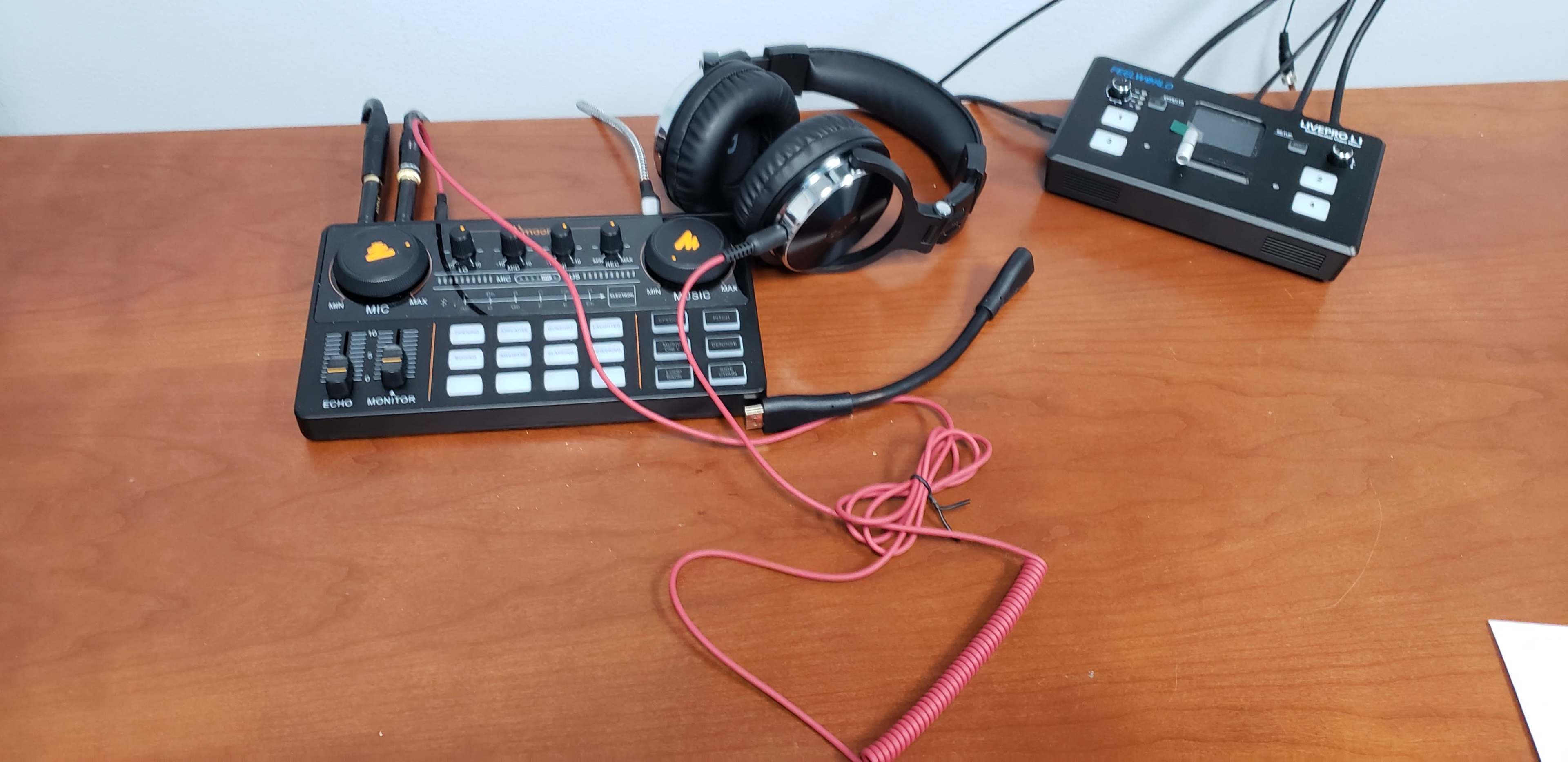 A black audio mixer with various controls is placed on a wooden table alongside headphones and a portable recording device.