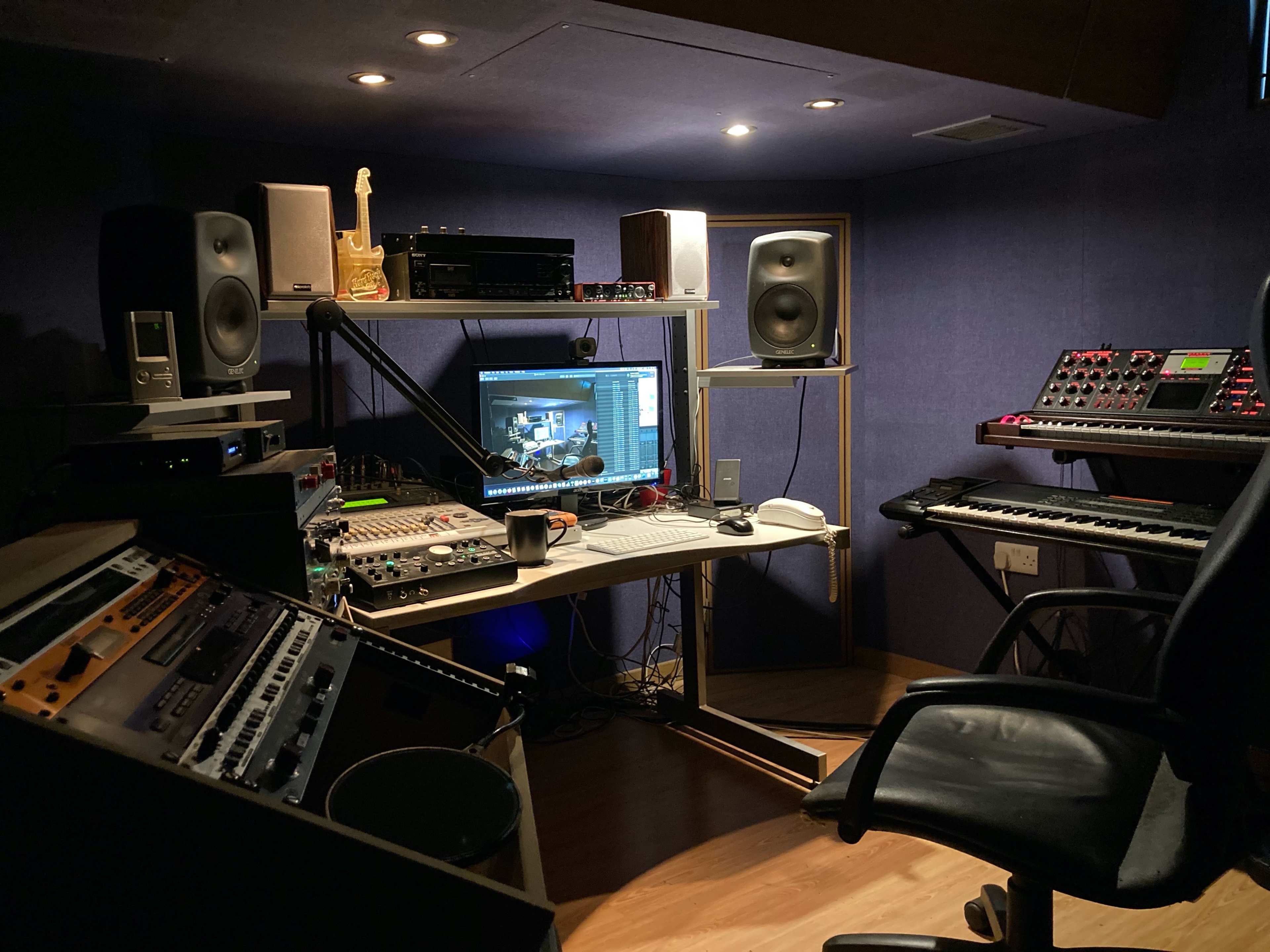 A music studio setup featuring a computer workstation, audio equipment, synthesizers, and studio monitors arranged in a compact space.