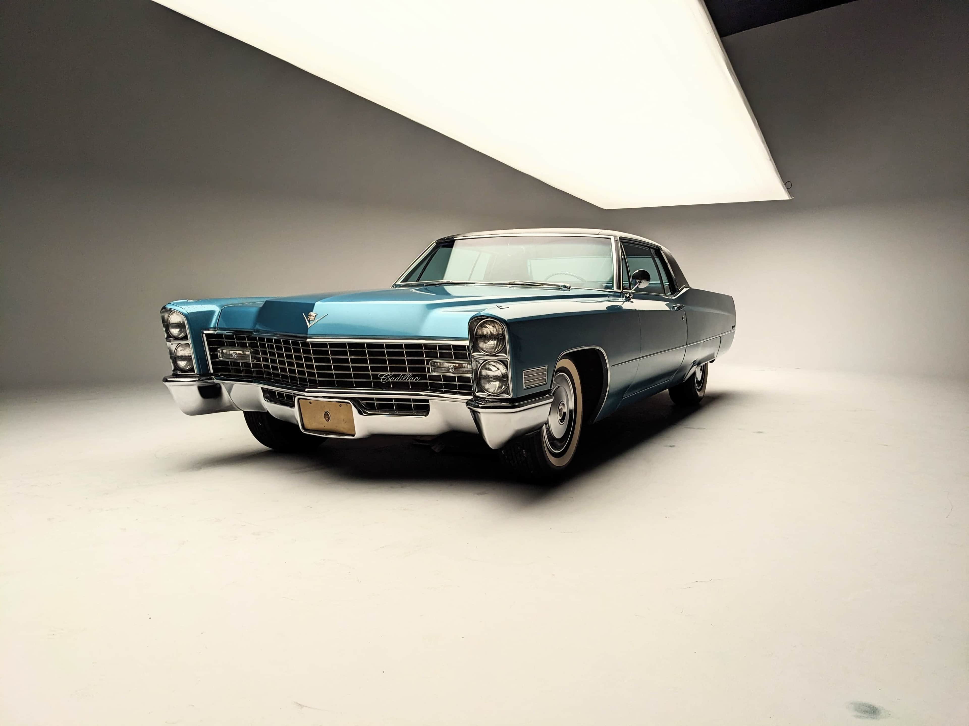 A vintage blue Cadillac is prominently displayed in a well-lit studio against a plain background.