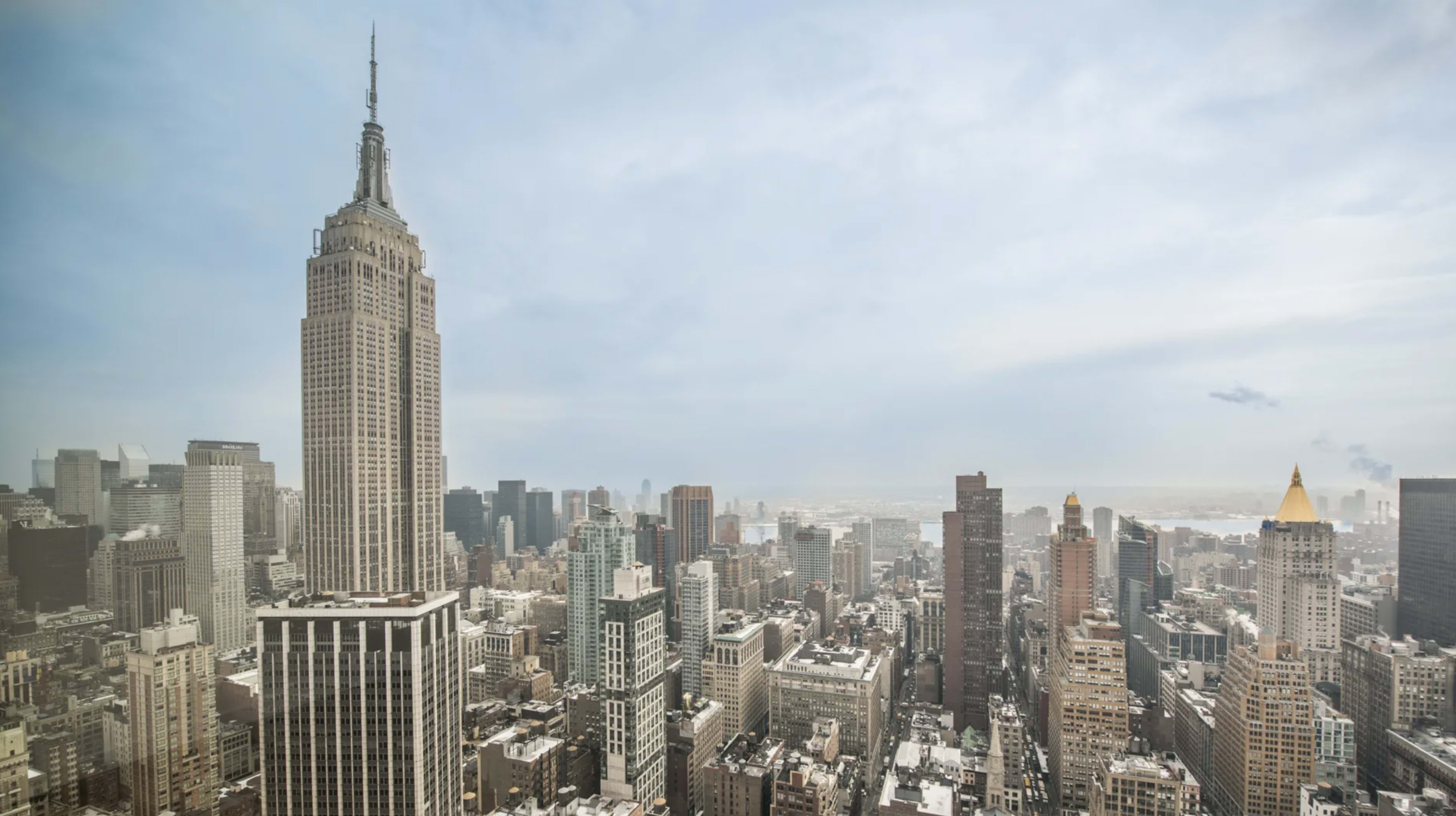 The image shows a panoramic view of New York City, highlighting the Empire State Building among a dense skyline of skyscrapers.
