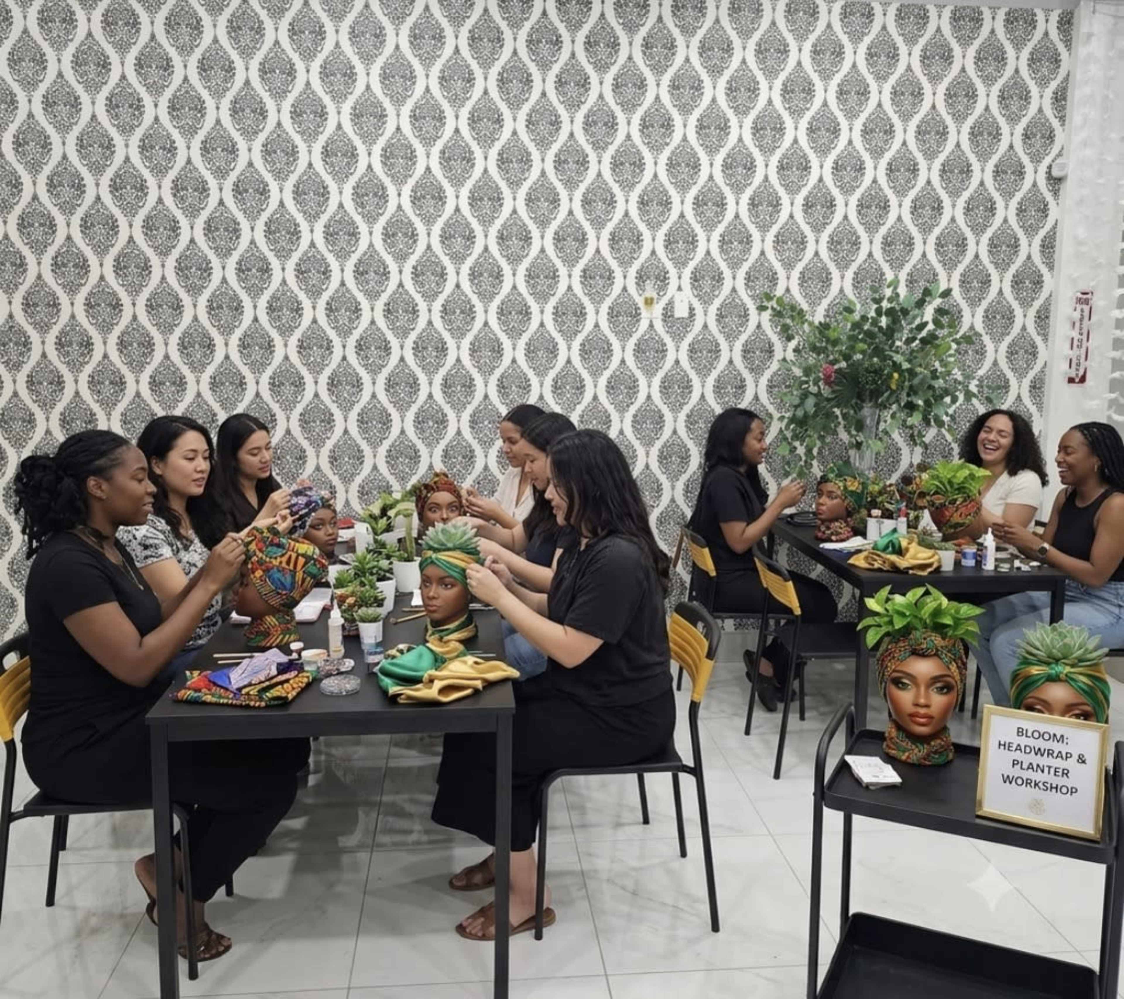 A group of women are seated around tables, engaged in a workshop focused on headwrap styling and planting, with decorative plants and vibrant fabrics present.