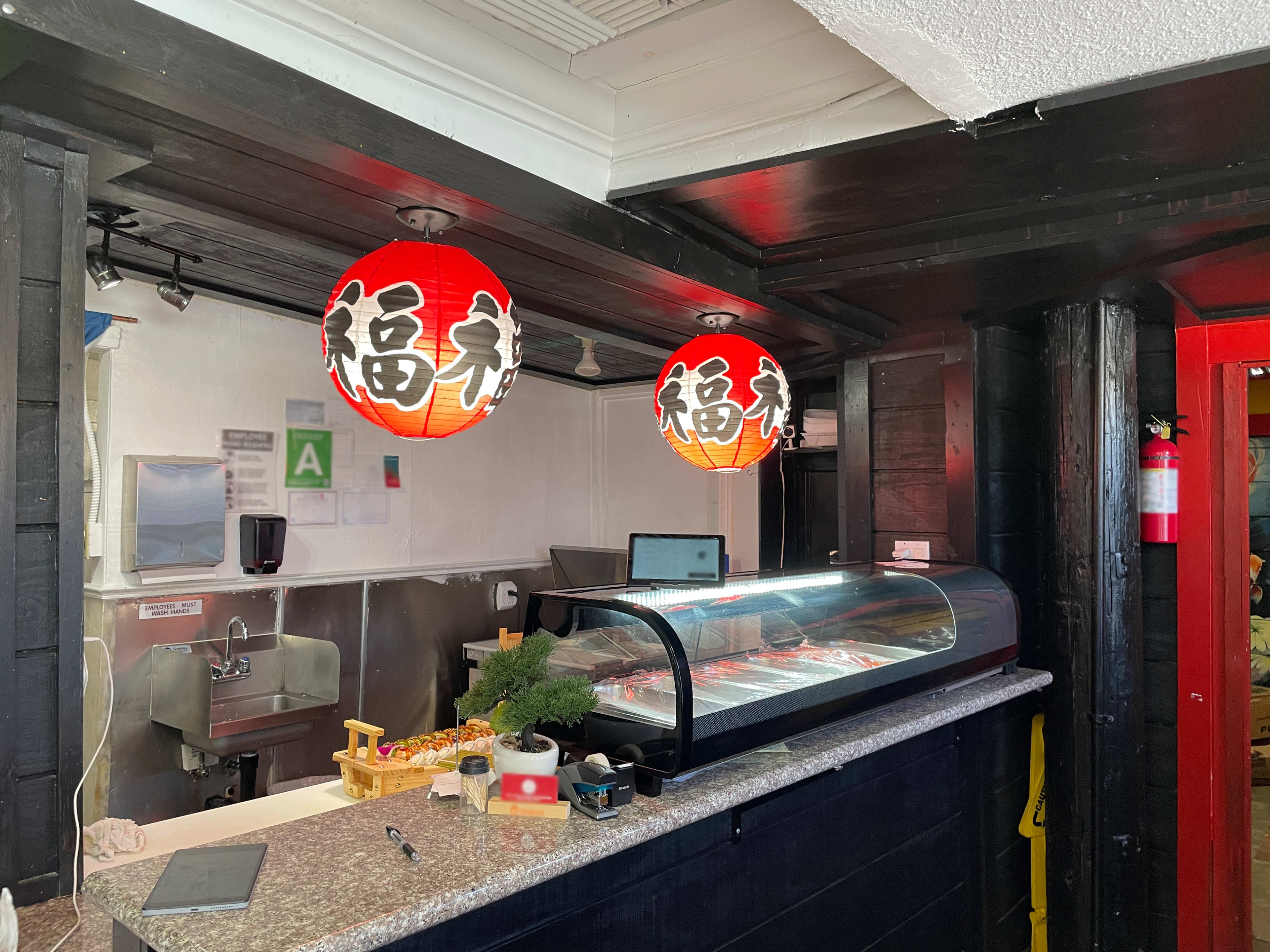 The image shows the interior of a sushi restaurant with two red paper lanterns hanging above a service counter.