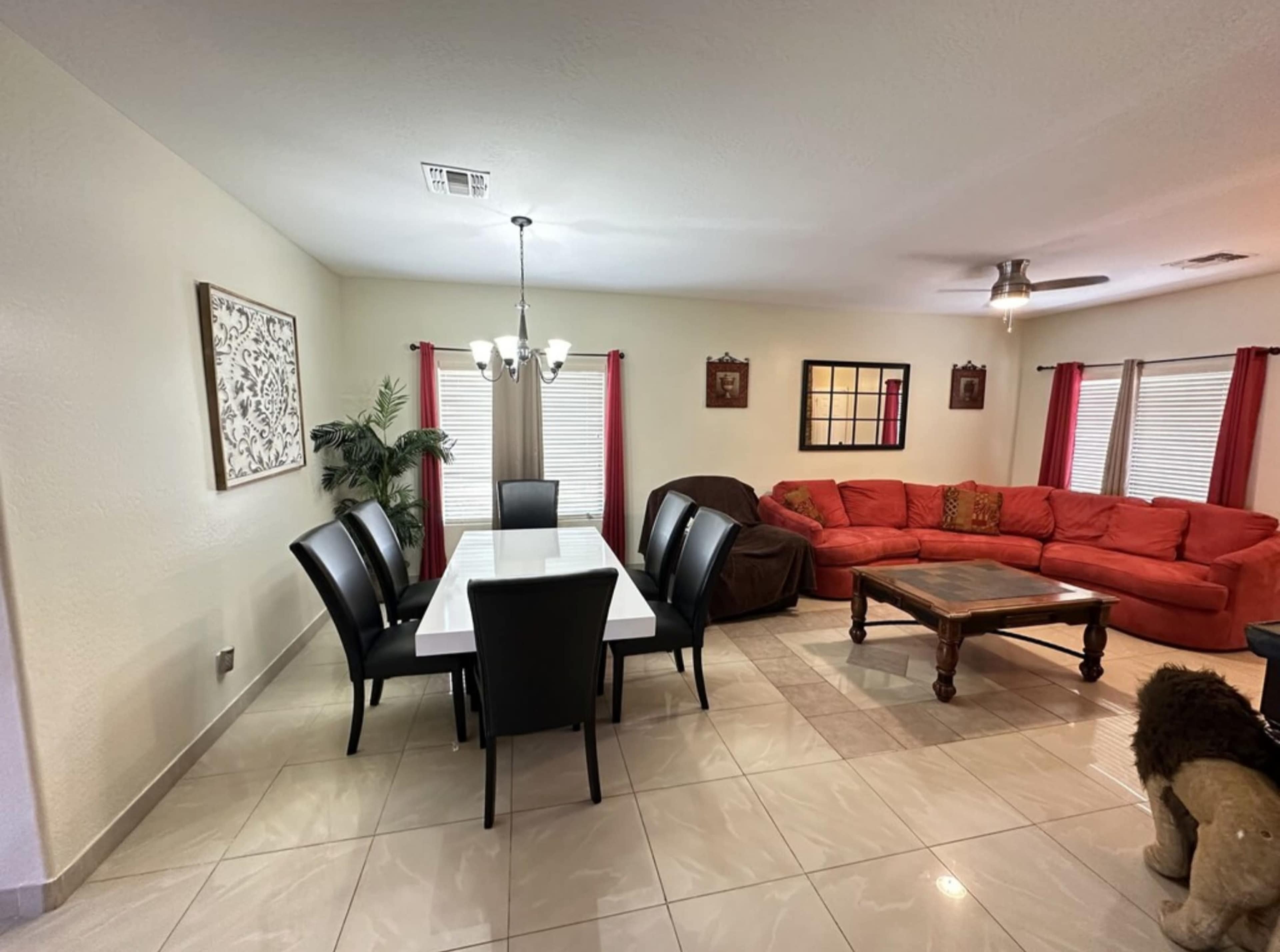 A dining table with black chairs is set next to a red sectional sofa in a light-colored living room.
