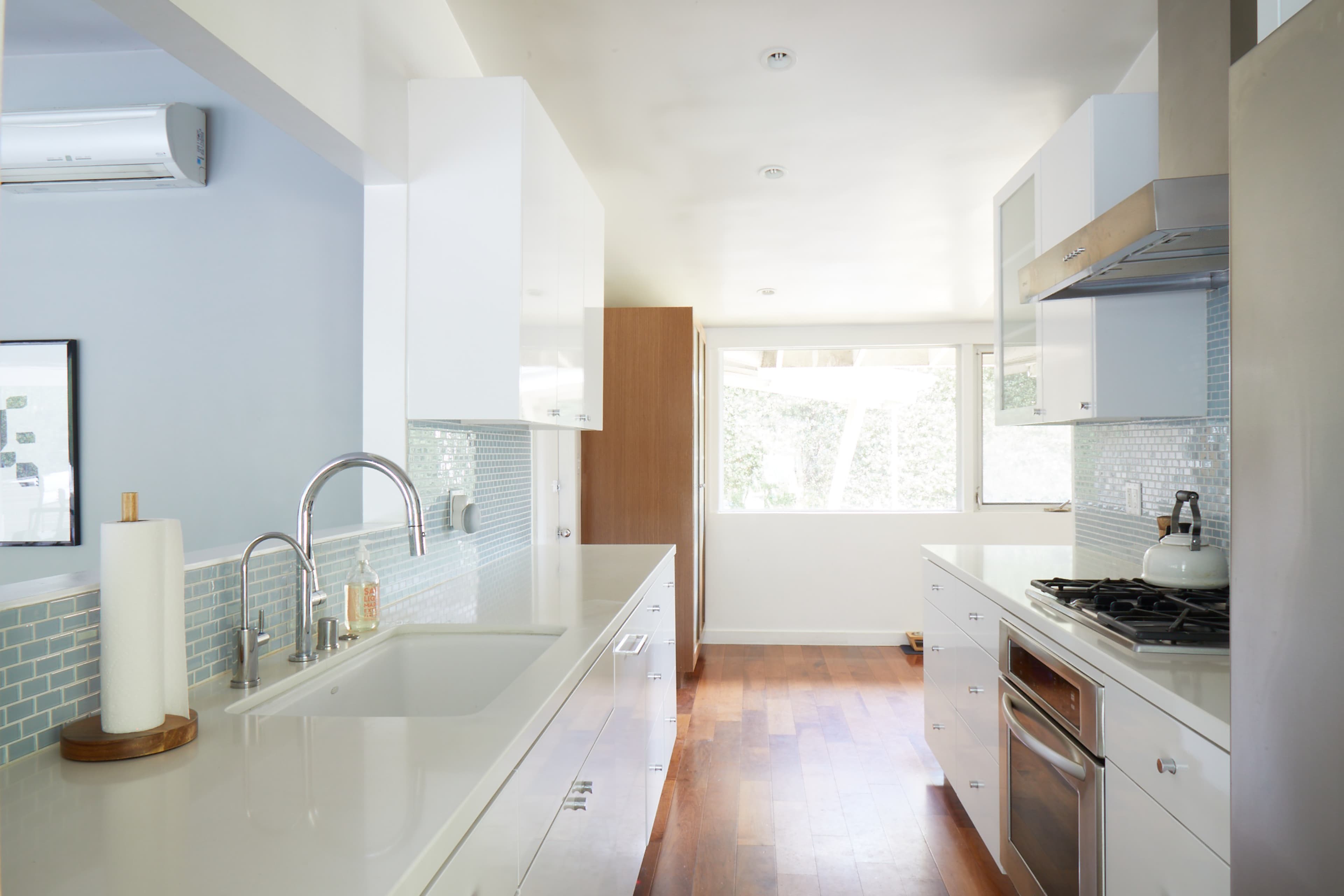 A modern kitchen features white cabinetry, a stainless steel stove, and a sink, with natural light coming through a large window.