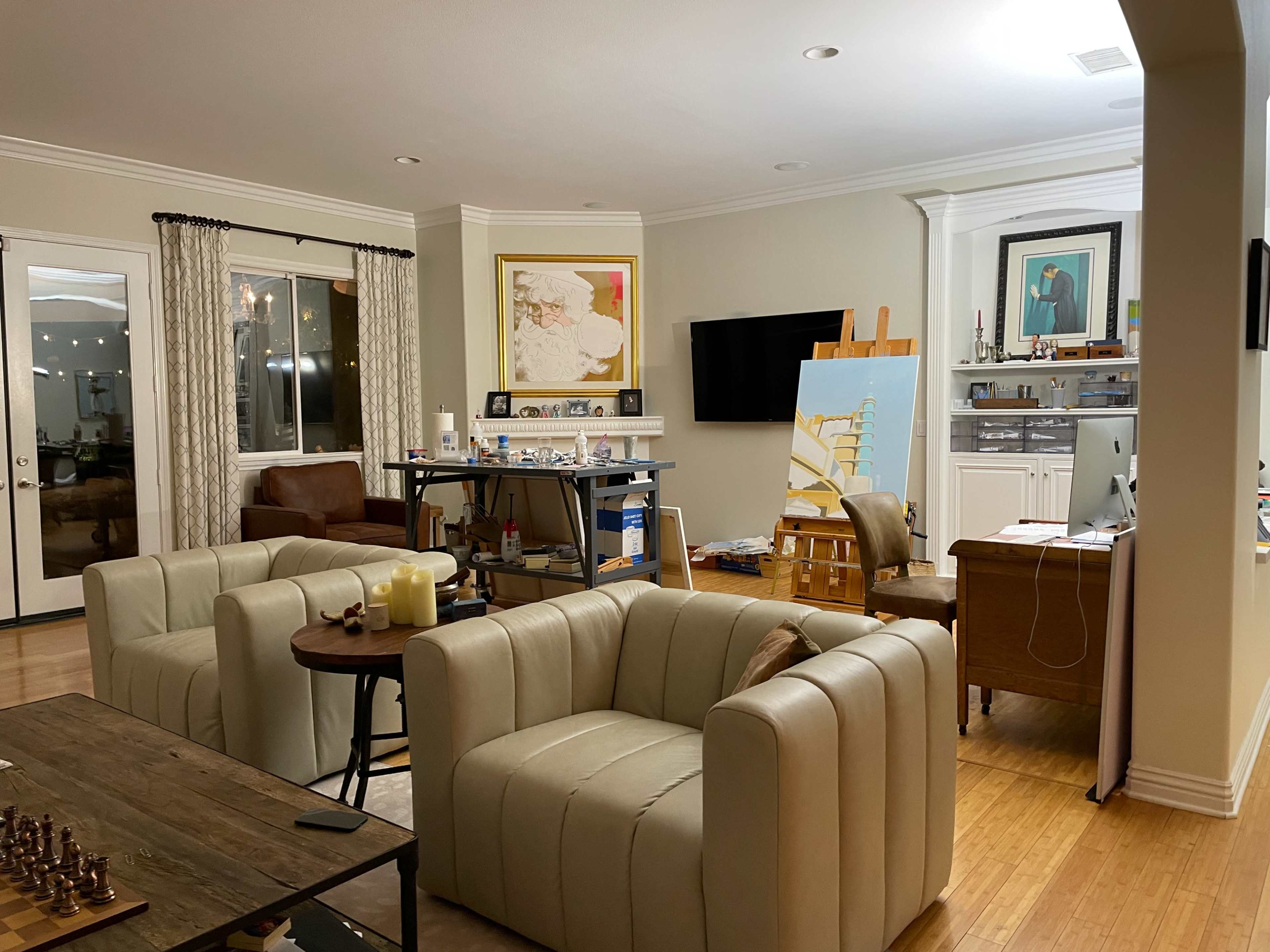 The image shows a well-furnished living room with two cream-colored armchairs, a chessboard on a wooden table, and various artworks displayed on the walls.