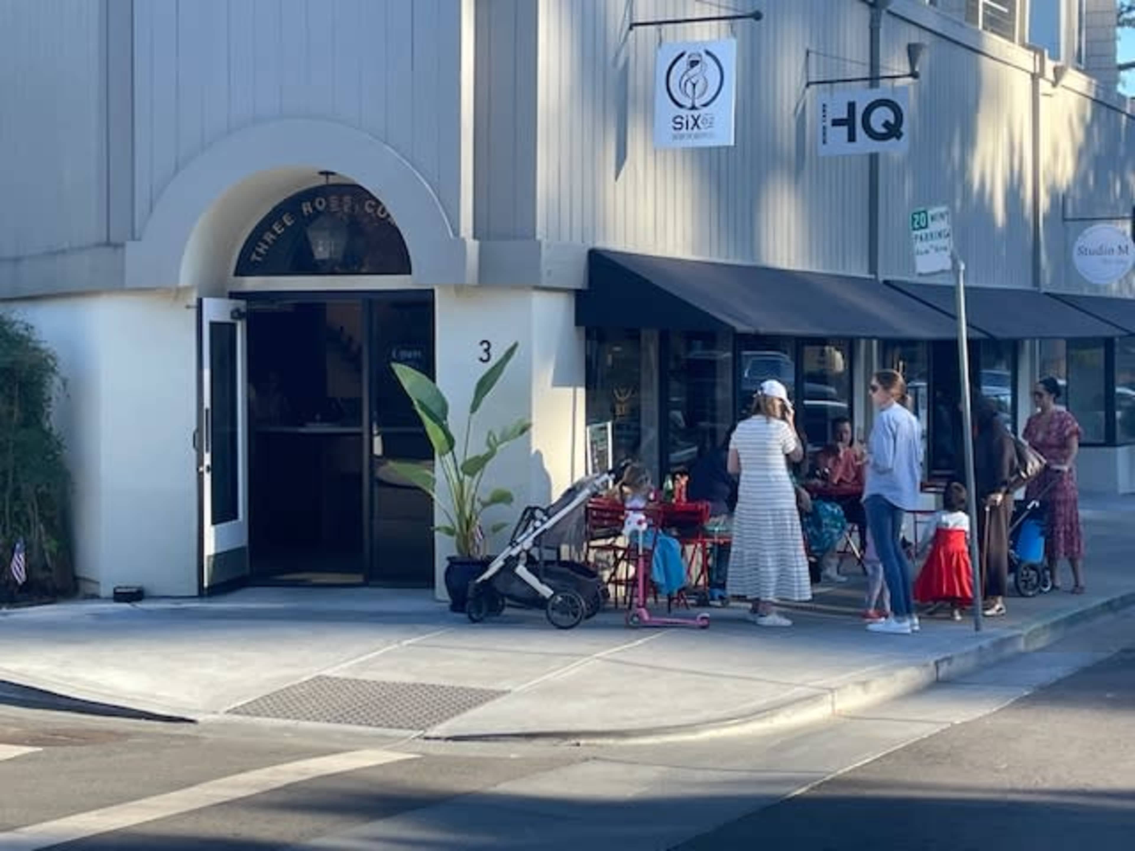 A group of people stands outside a storefront with an arched entrance while strollers are parked nearby.