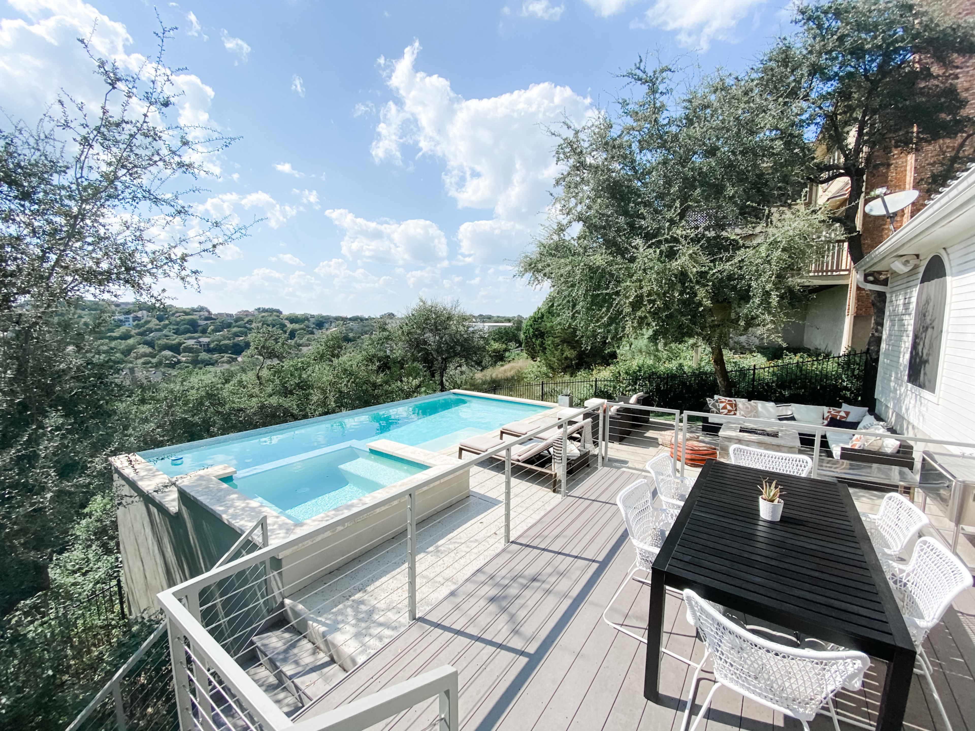 A modern outdoor deck with a swimming pool, surrounded by trees and a scenic view.