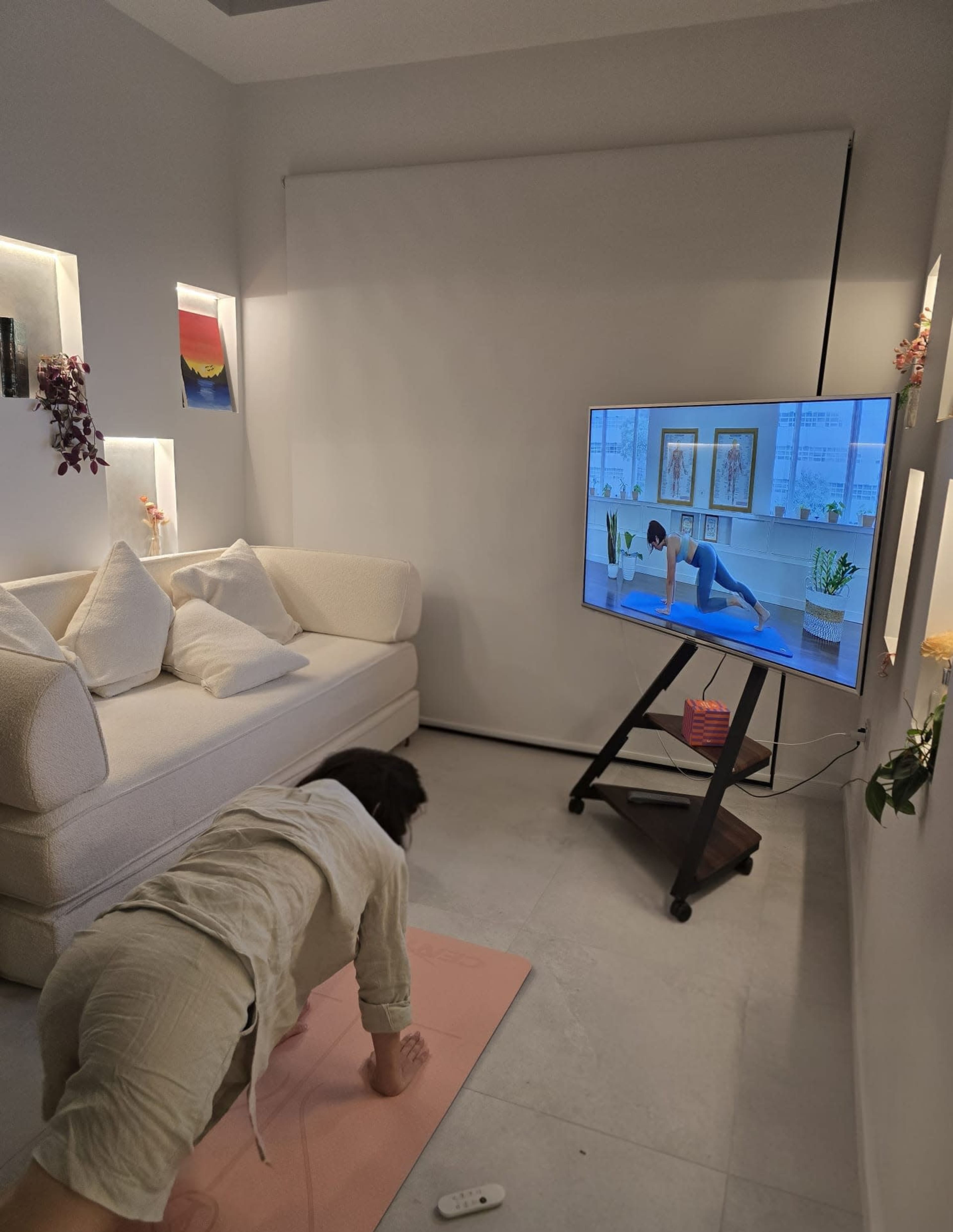 A person is exercising on a yoga mat in a stylish living room while following a workout video displayed on a television.