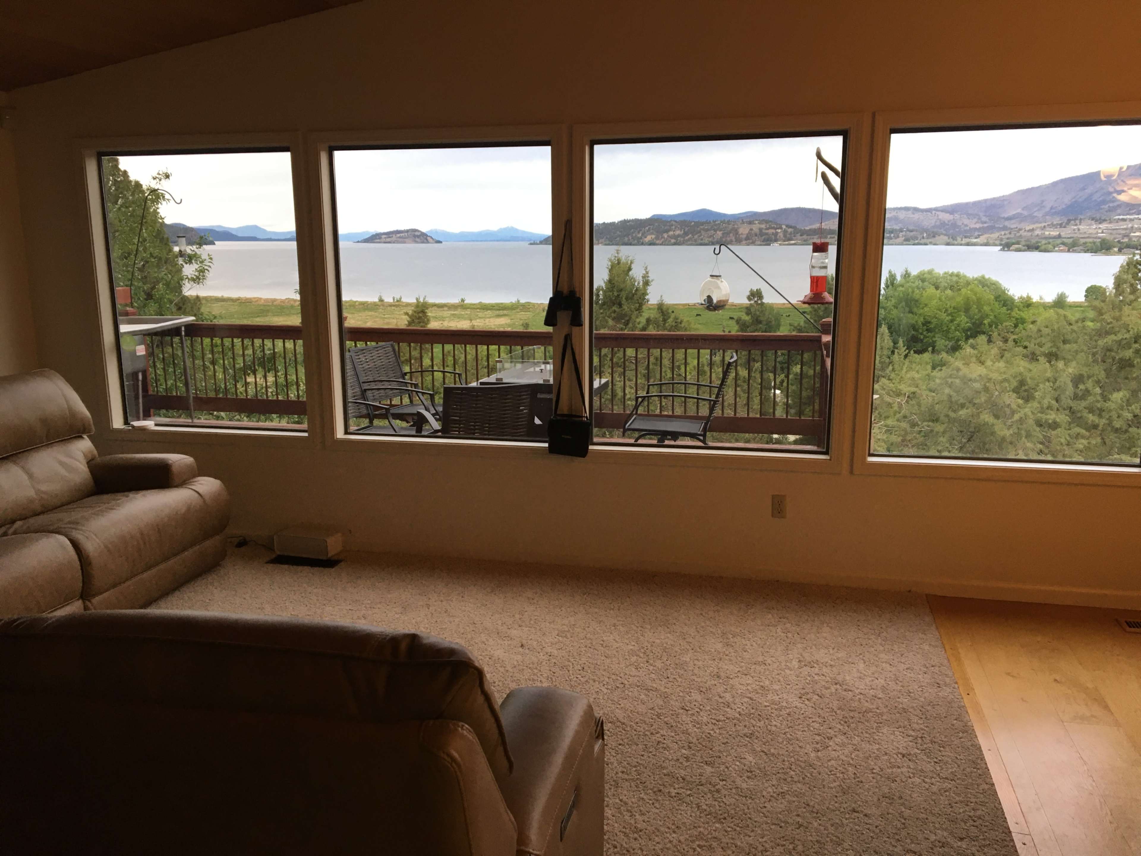 A living room with a beige couch overlooks a scenic view of a lake framed by large windows.