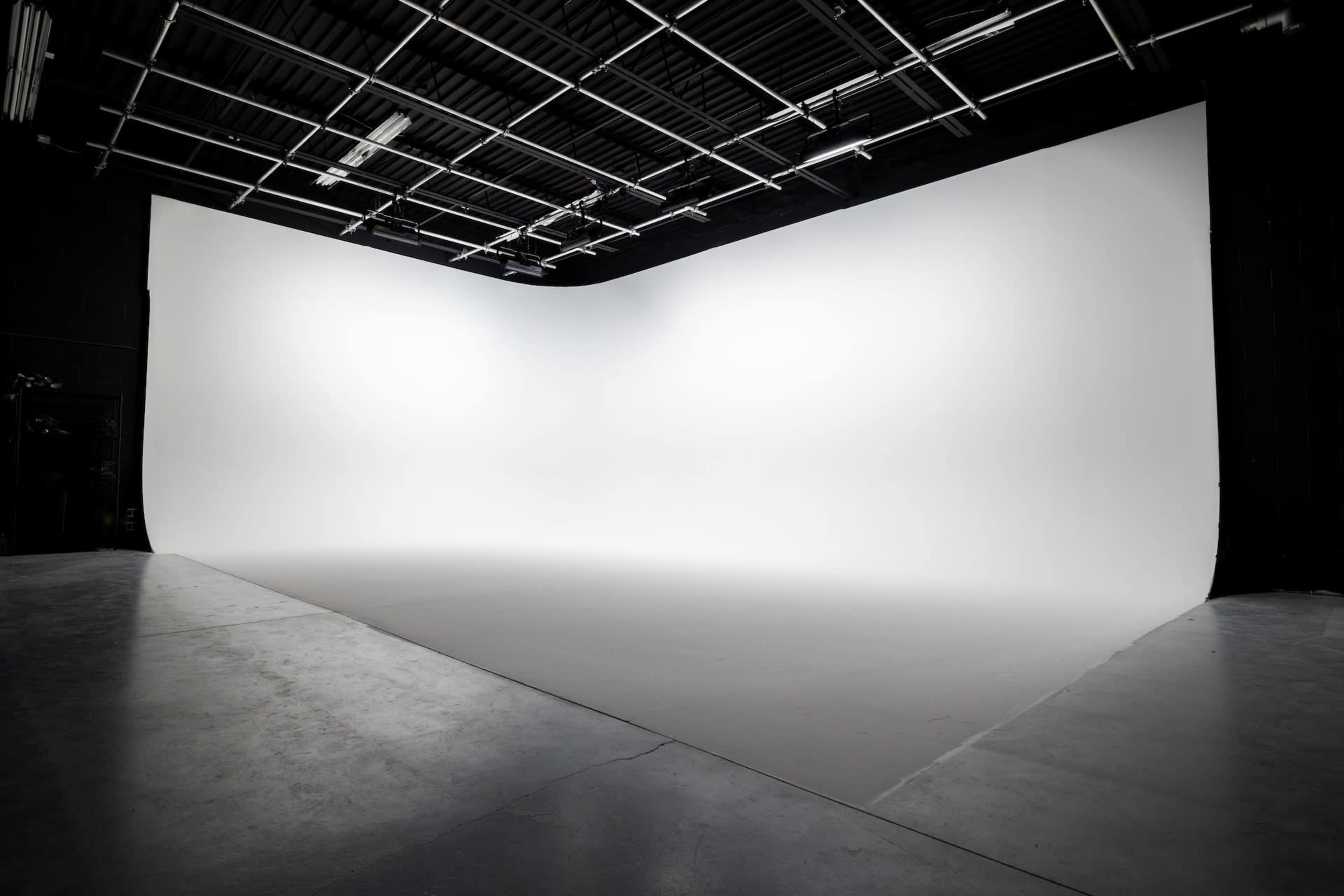 A spacious photography studio with a seamless white backdrop and a clean, empty floor.