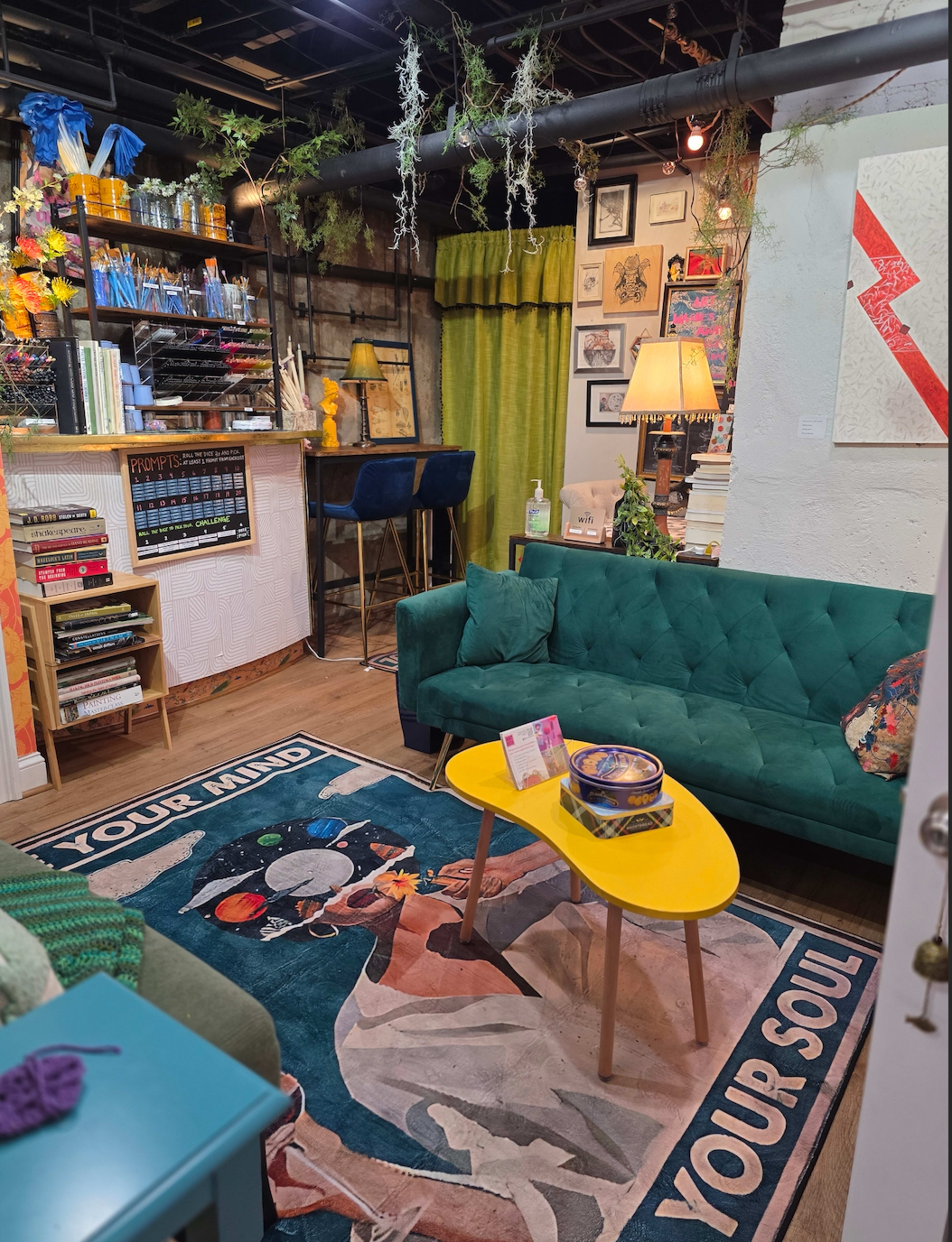 The image features a cozy indoor space with a green sofa, a yellow coffee table, and various artworks on the walls, illuminated by a lamp.