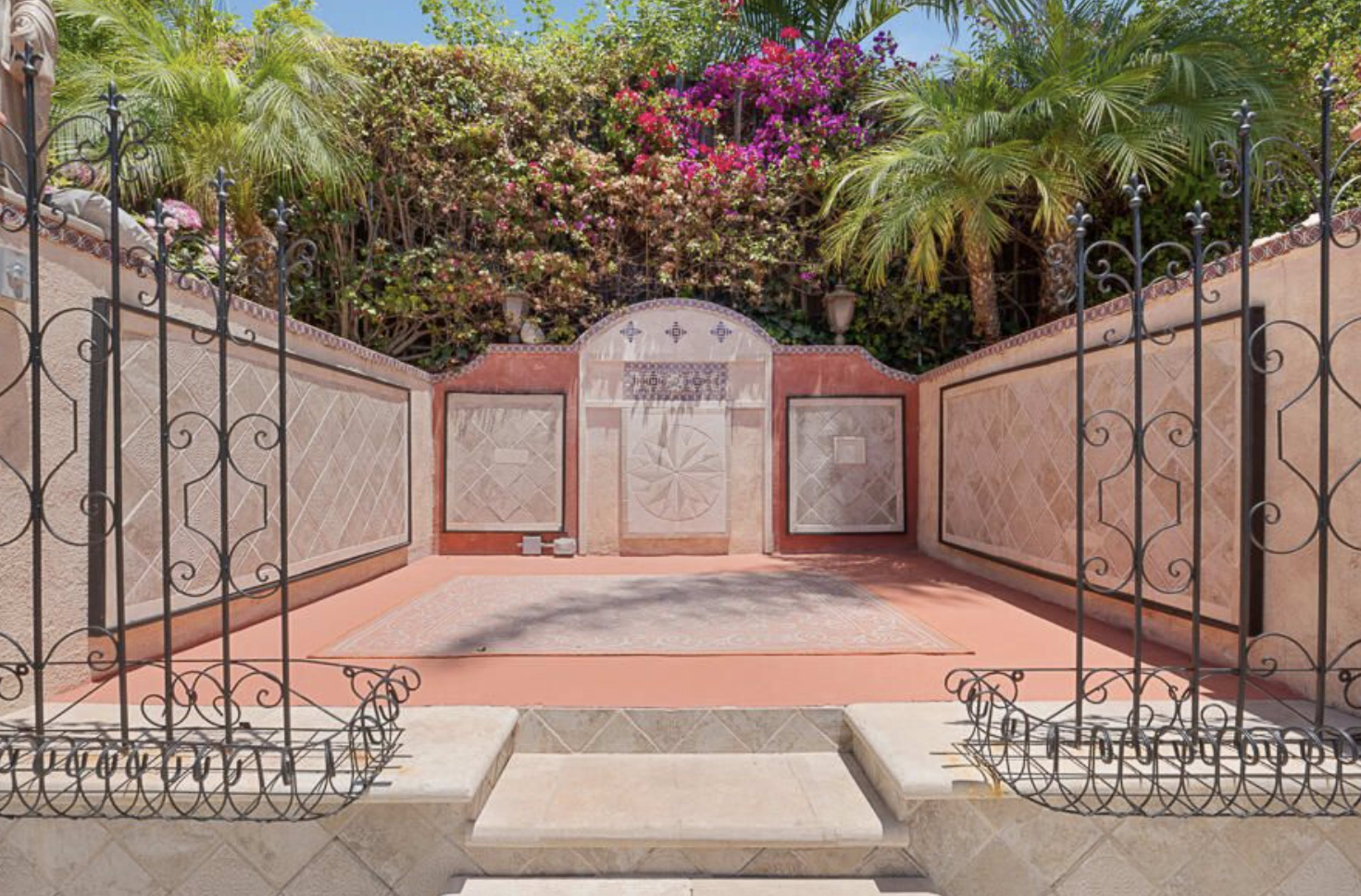 A walled courtyard with decorative stone walls, potted plants, and a patterned tile floor.