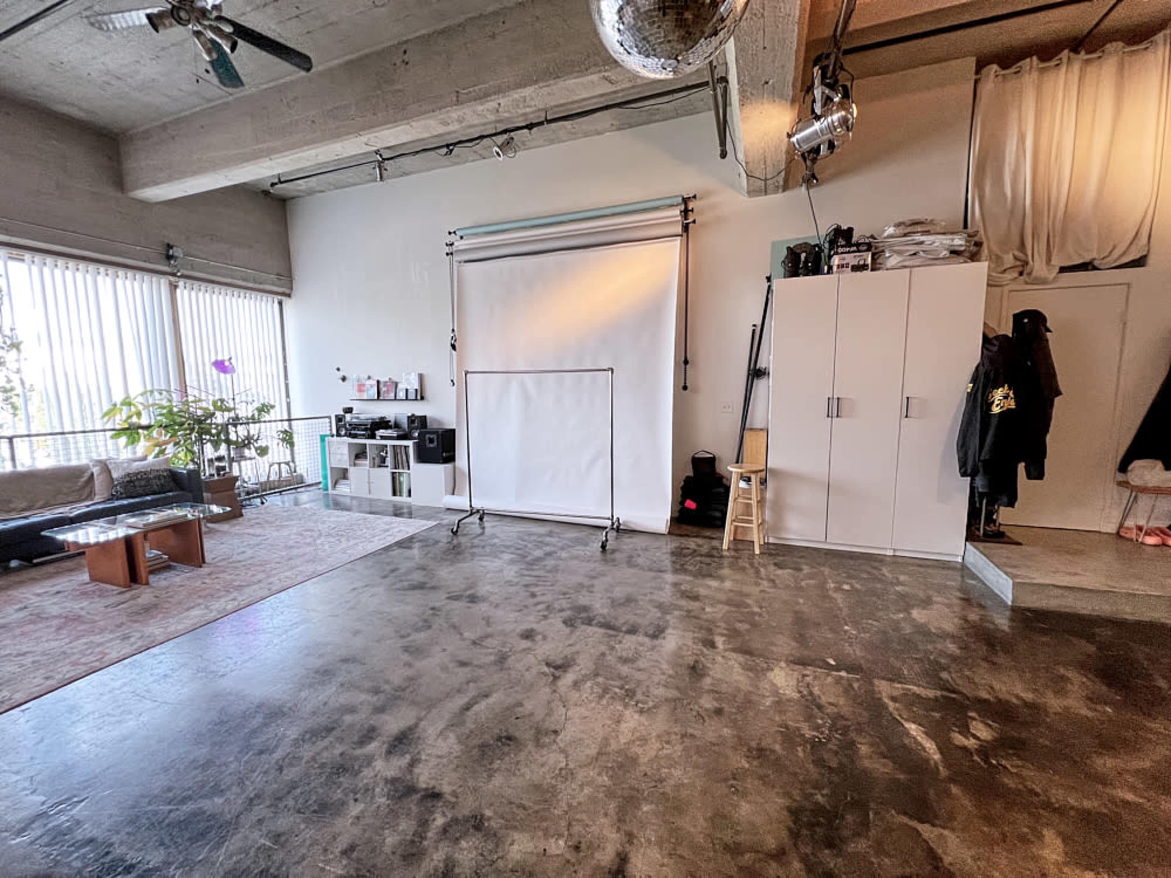 A spacious, minimalist interior with a concrete floor, a backdrop setup, and furniture along the sides.