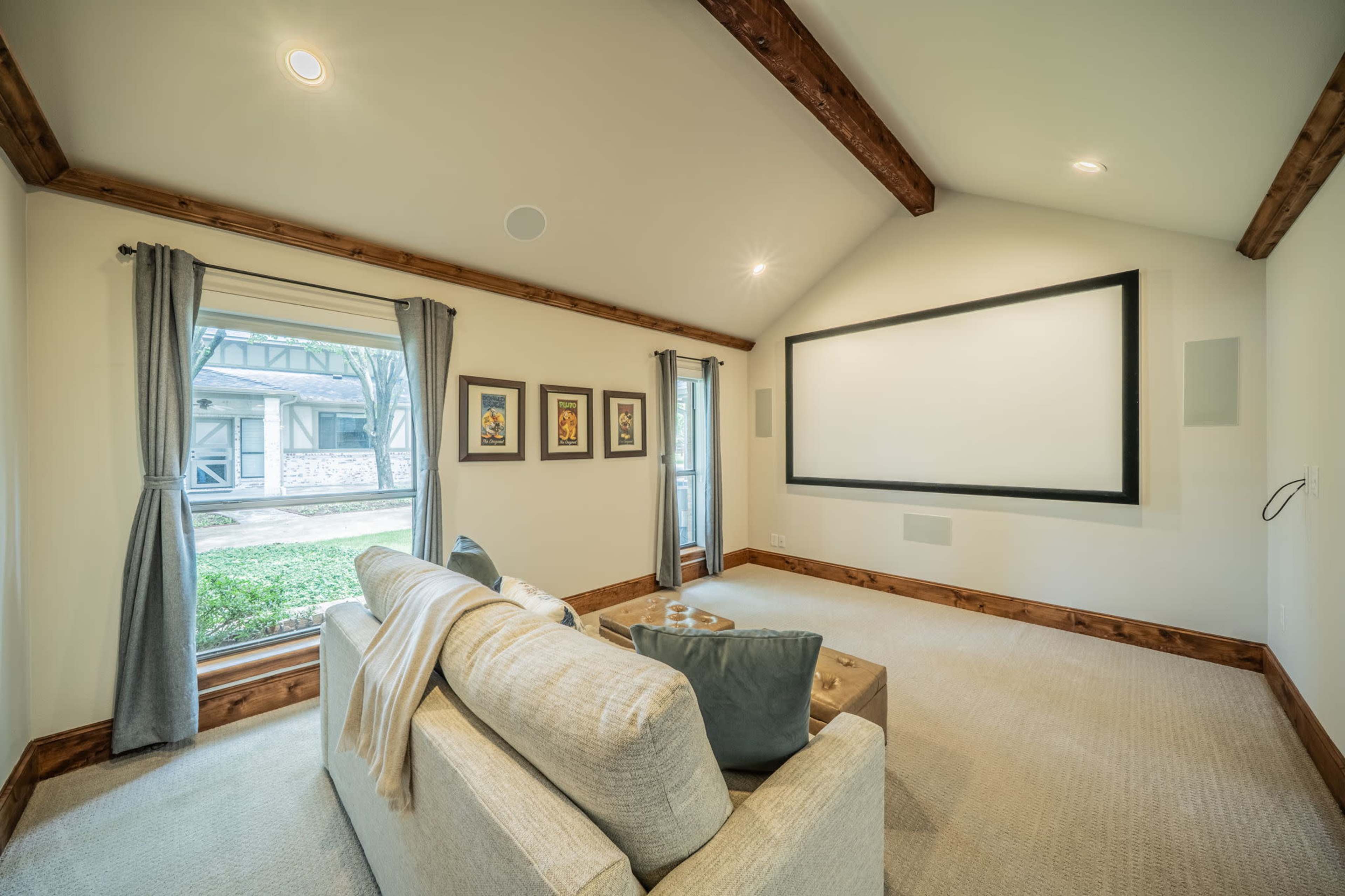 The image shows a cozy home theater room with a large screen, comfortable seating, and framed artwork on the walls.