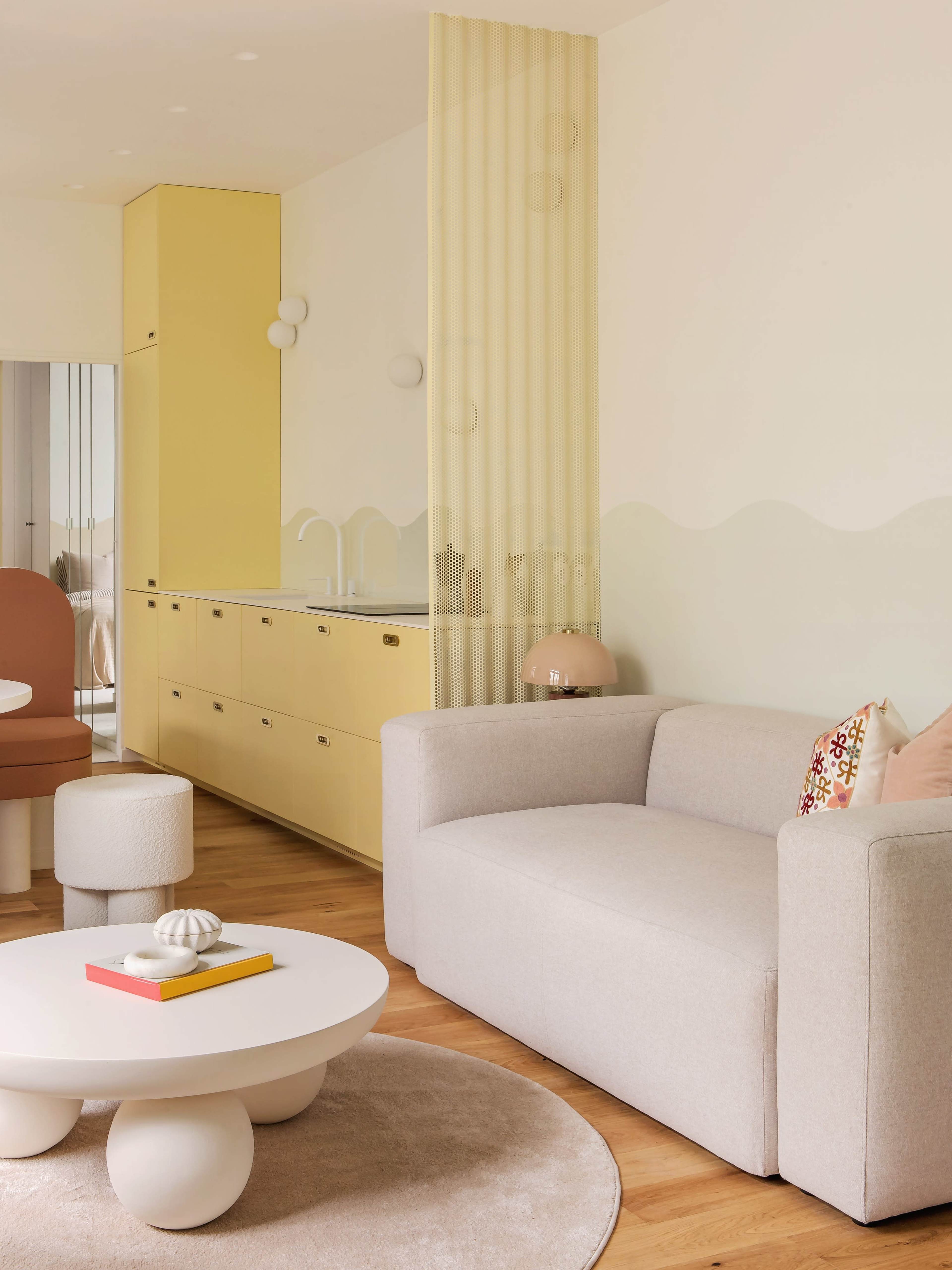 The image shows a modern living room featuring a light-colored sofa, a round coffee table, and a yellow cabinetry section with a transparent divider in the background.