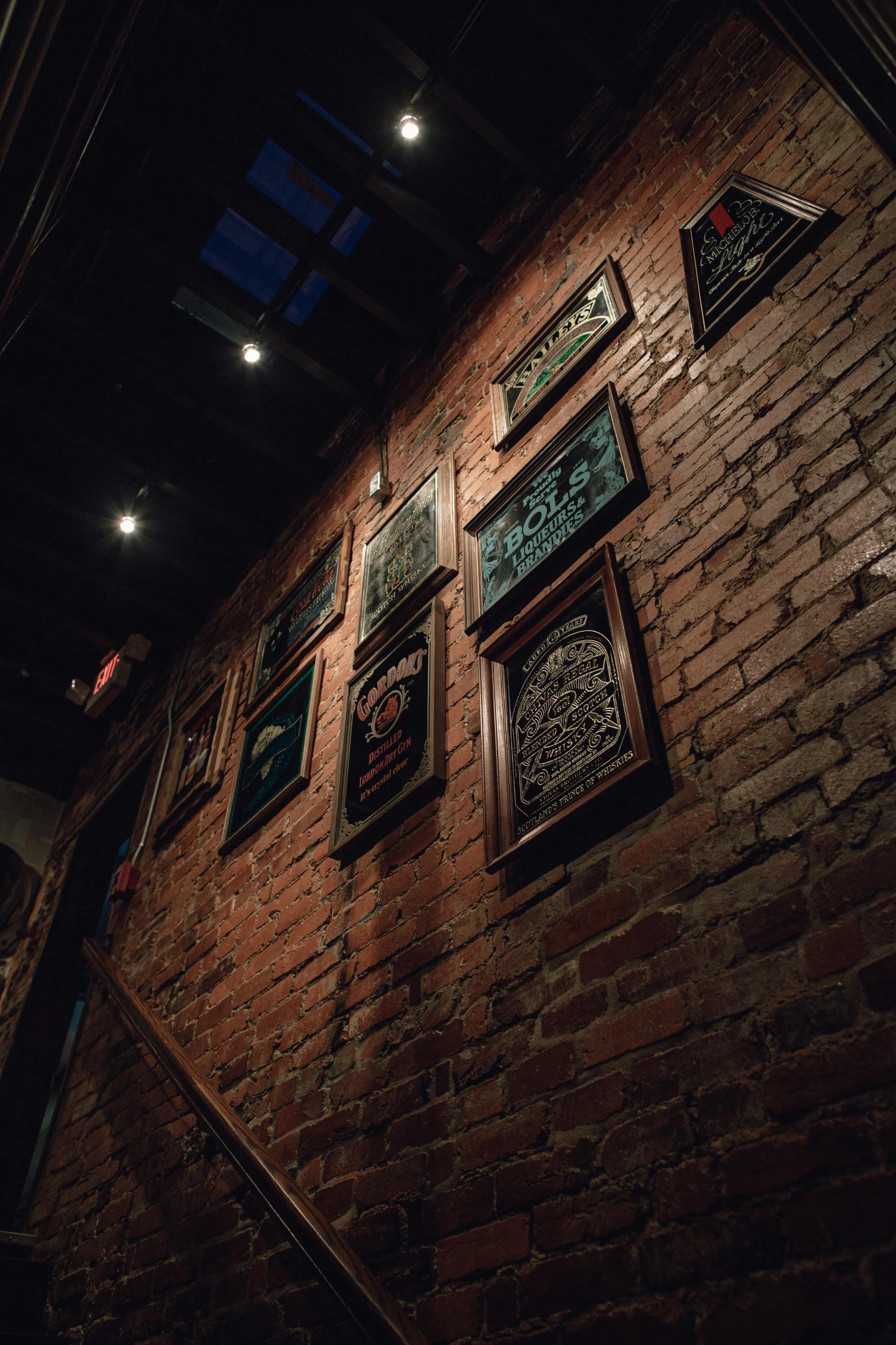 A dimly lit stairwell with a brick wall adorned with framed signs and artwork.