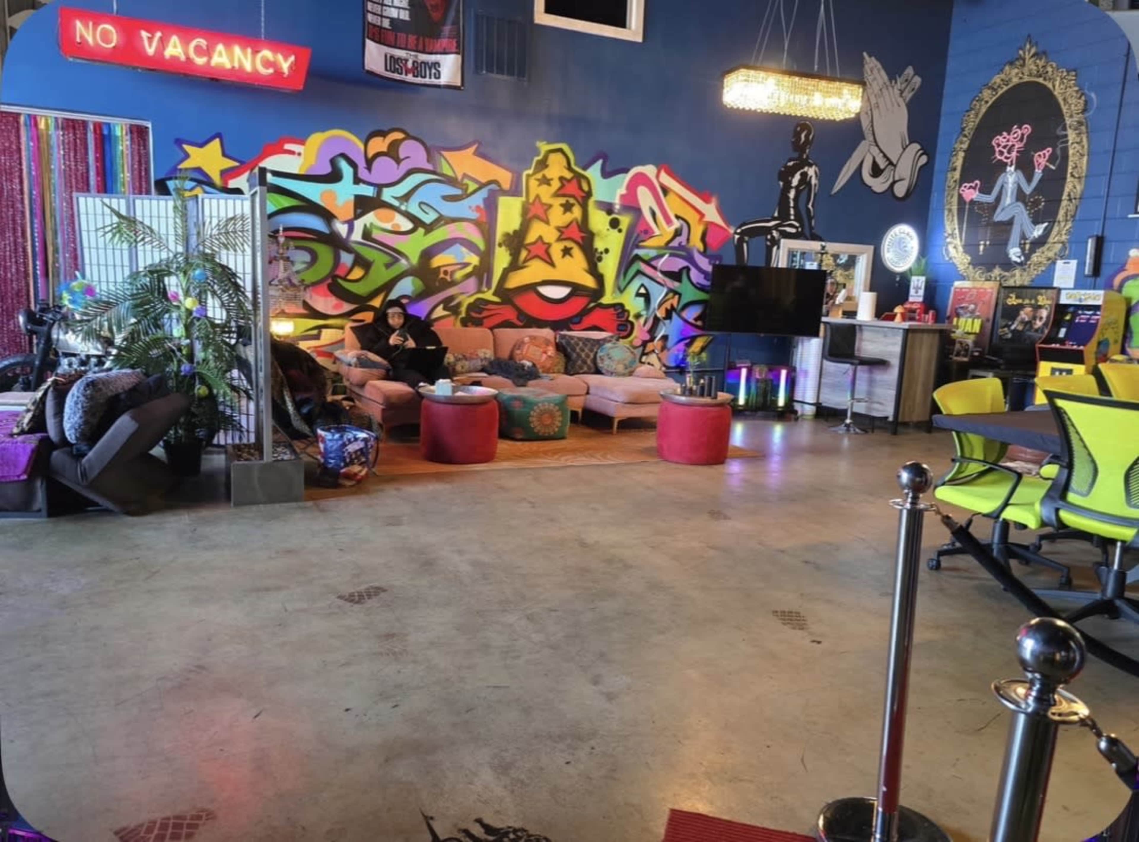 The image shows a colorful indoor lounge area featuring a vibrant graffiti wall, modern furniture, and various decorations.