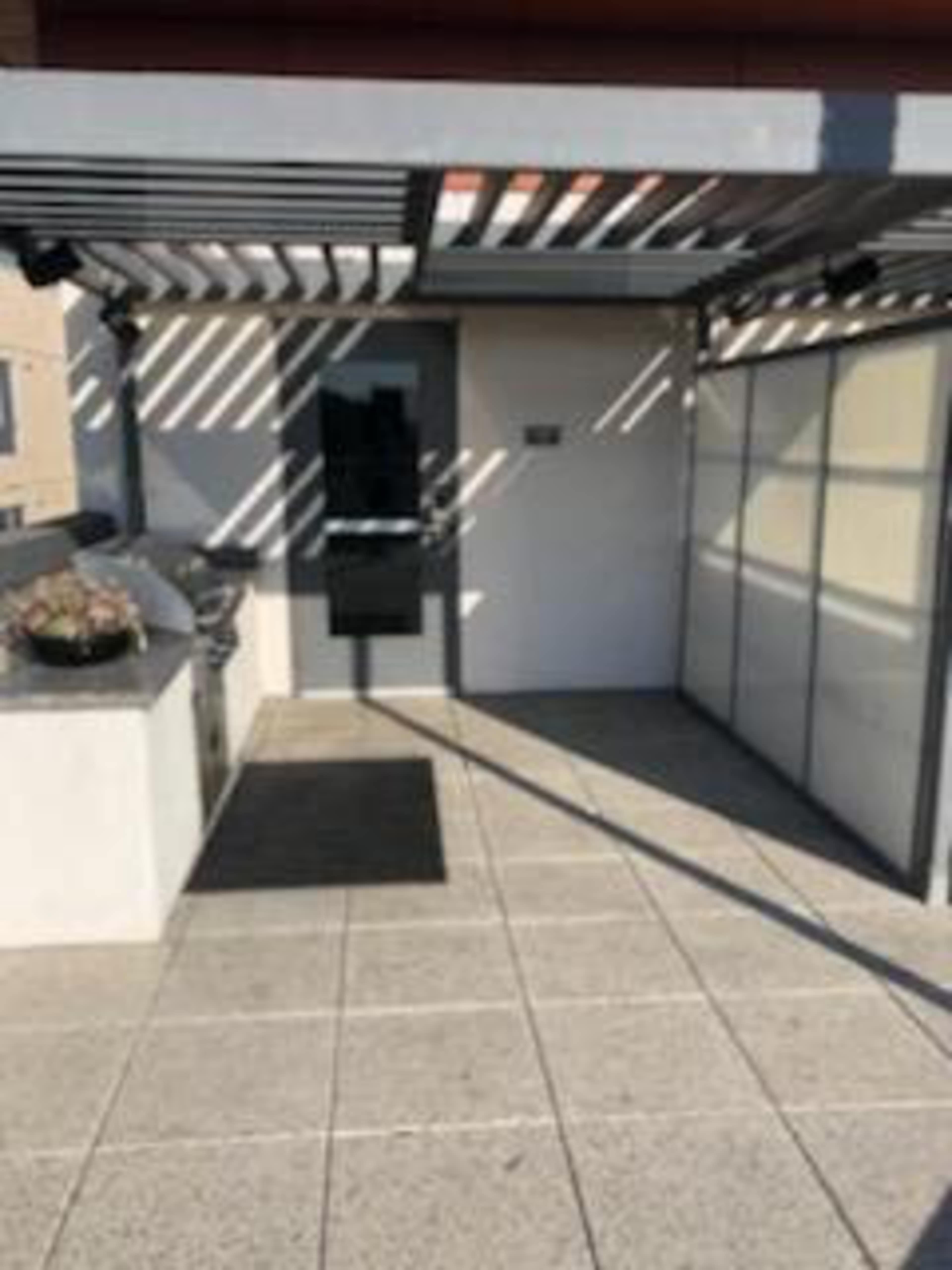An outdoor area with a grill, a paved floor, and a door under a striped awning.