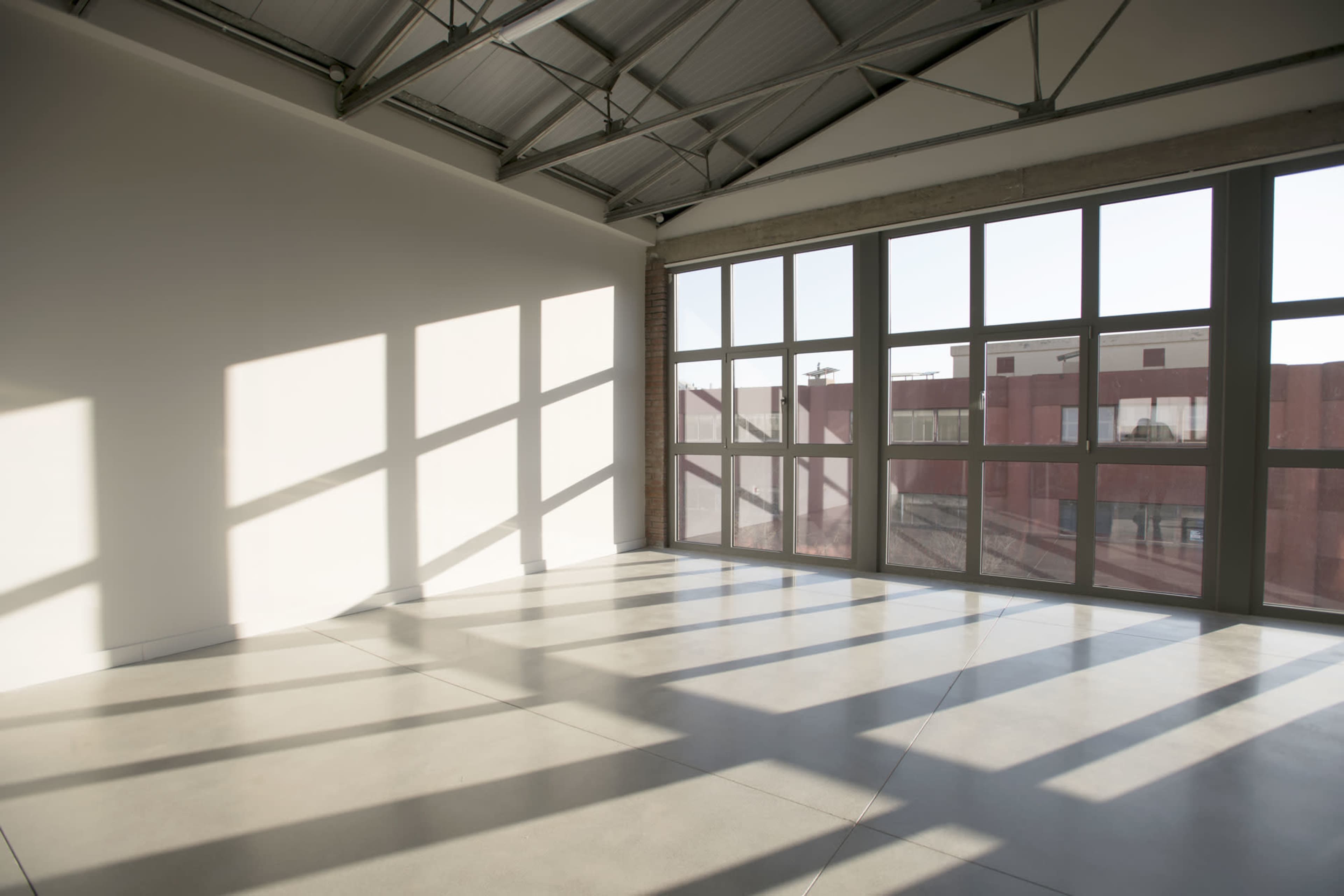 A spacious interior room features large windows casting geometric shadows on the polished concrete floor.