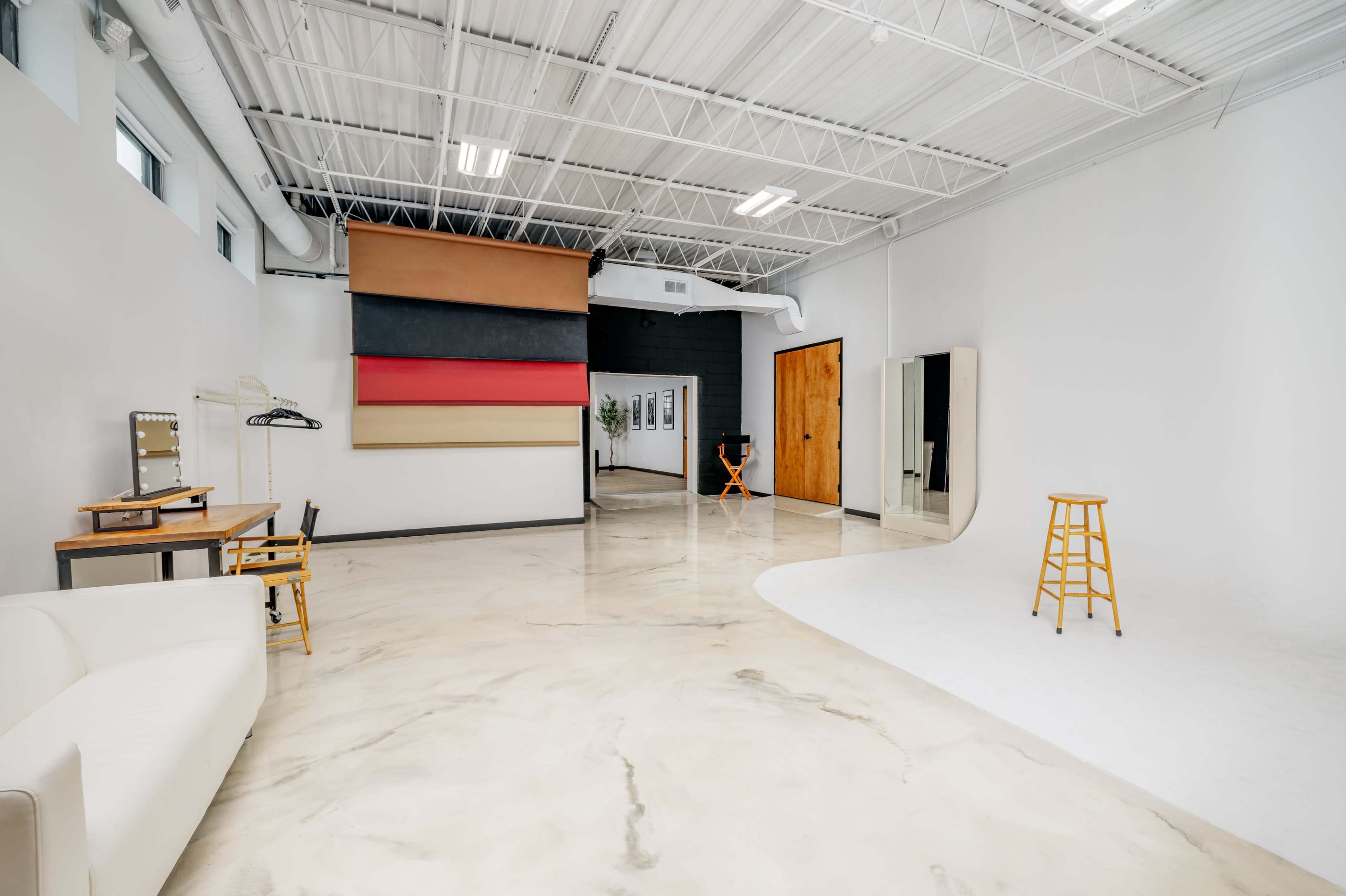 A spacious photography studio featuring a seamless backdrop, a seating area, and a changing room.