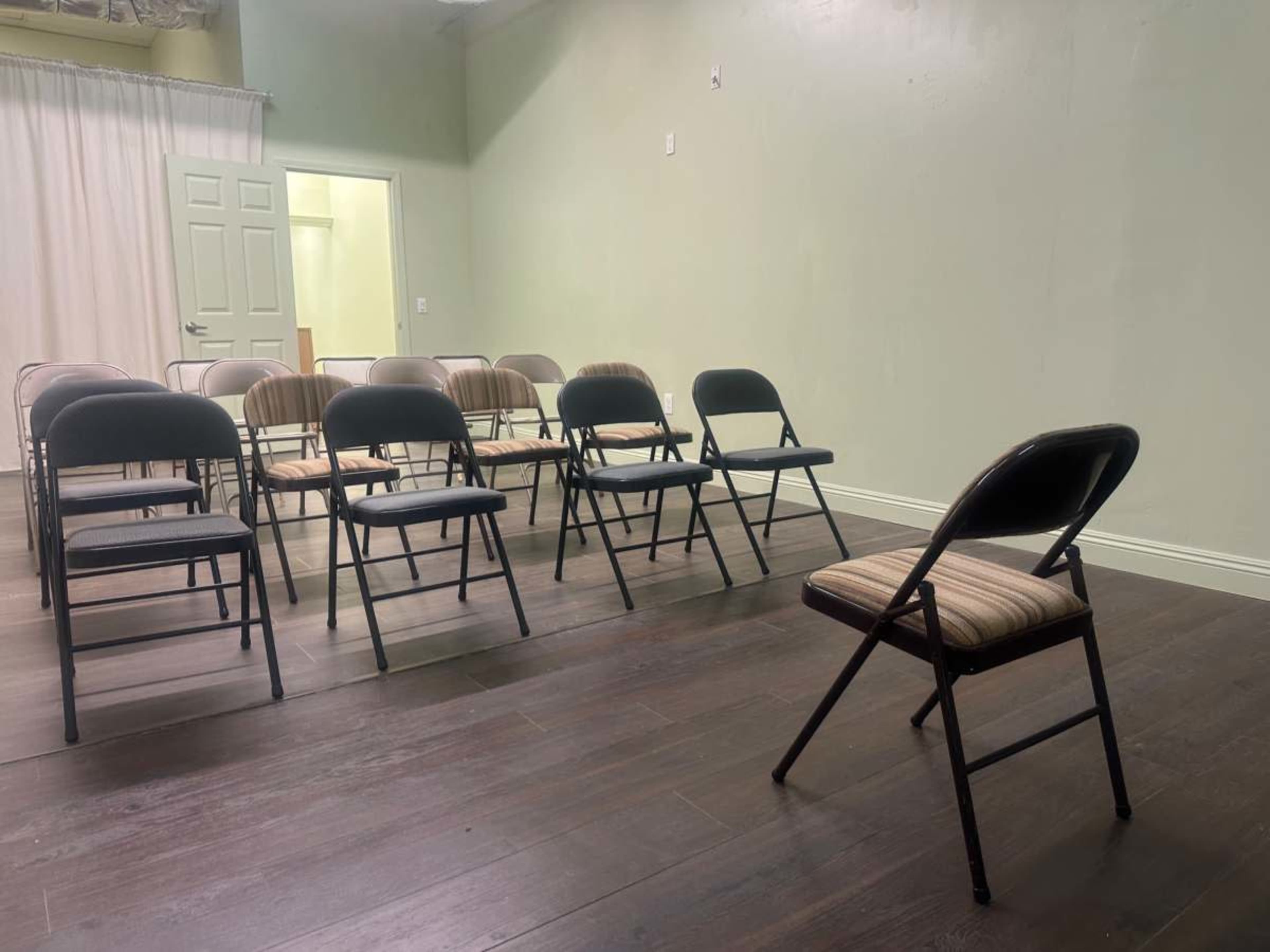 The image shows a room with a series of folding chairs arranged in rows, with one chair placed slightly apart from the others.