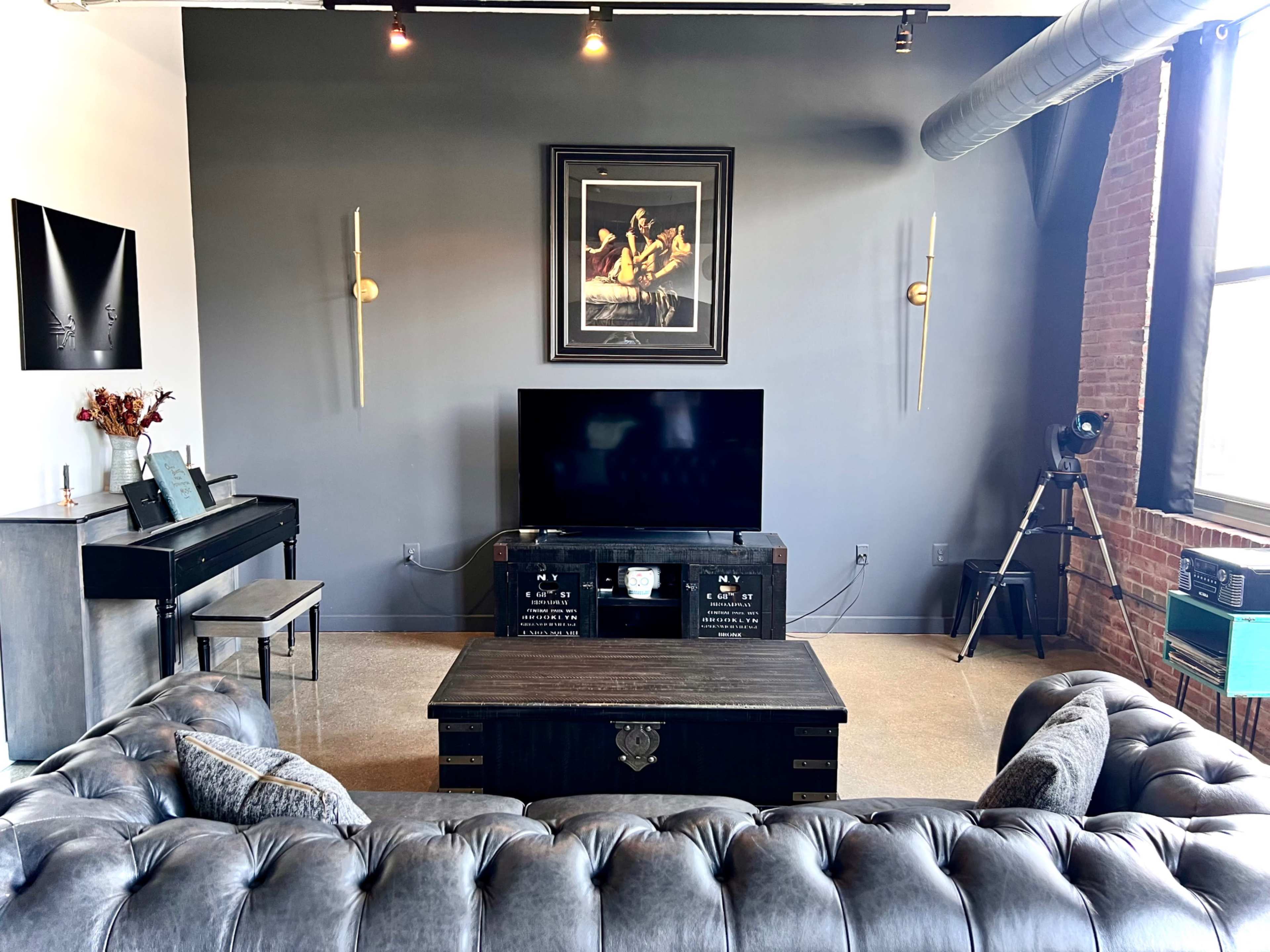 A modern living room featuring a dark gray wall, a large flat-screen TV on a media console, a coffee table, a tufted sofa, and a vintage-style camera on a tripod.