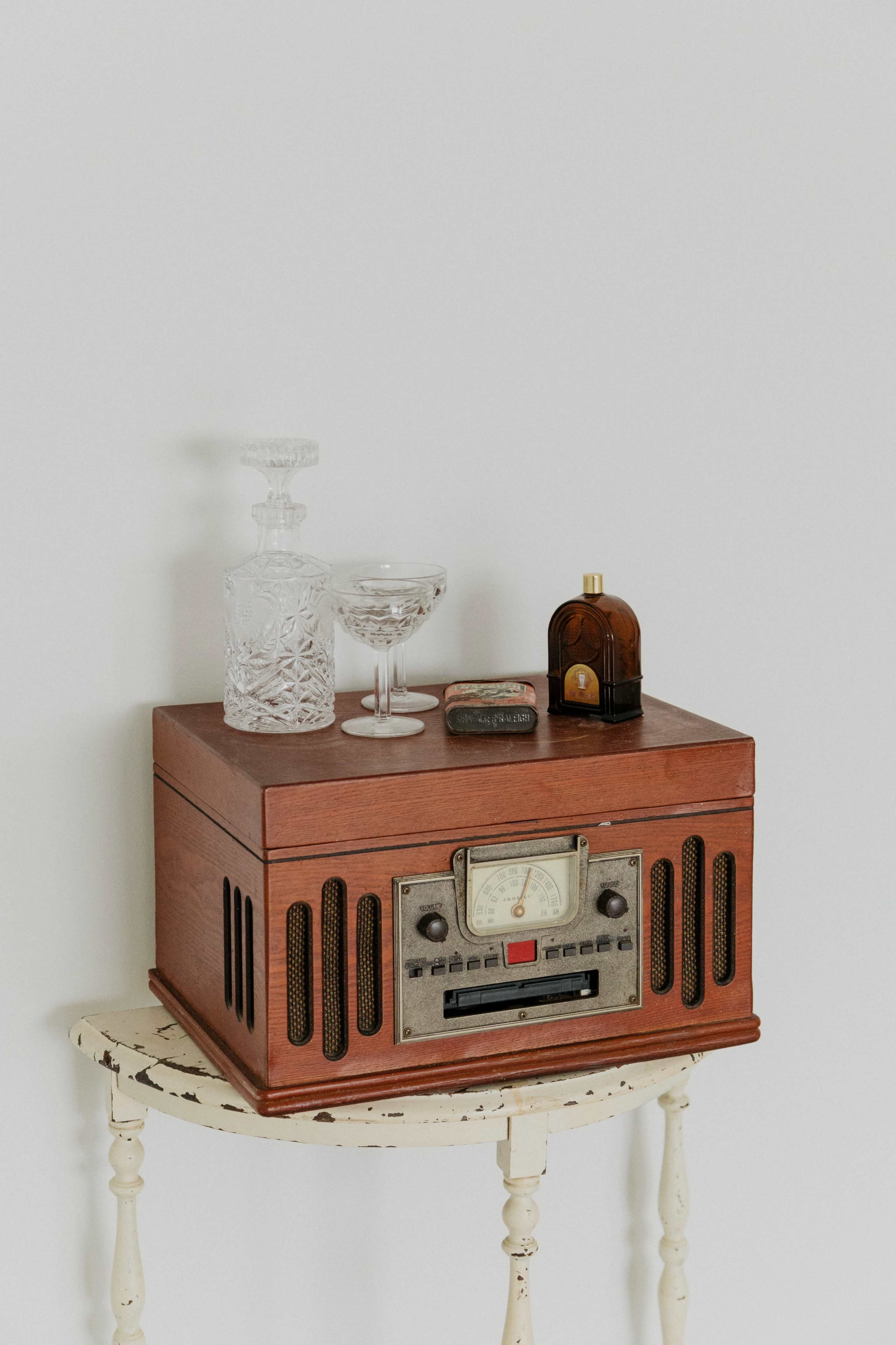 A vintage wooden radio sits on a small table, accompanied by a crystal decanter, a glass, and a decorative bottle.