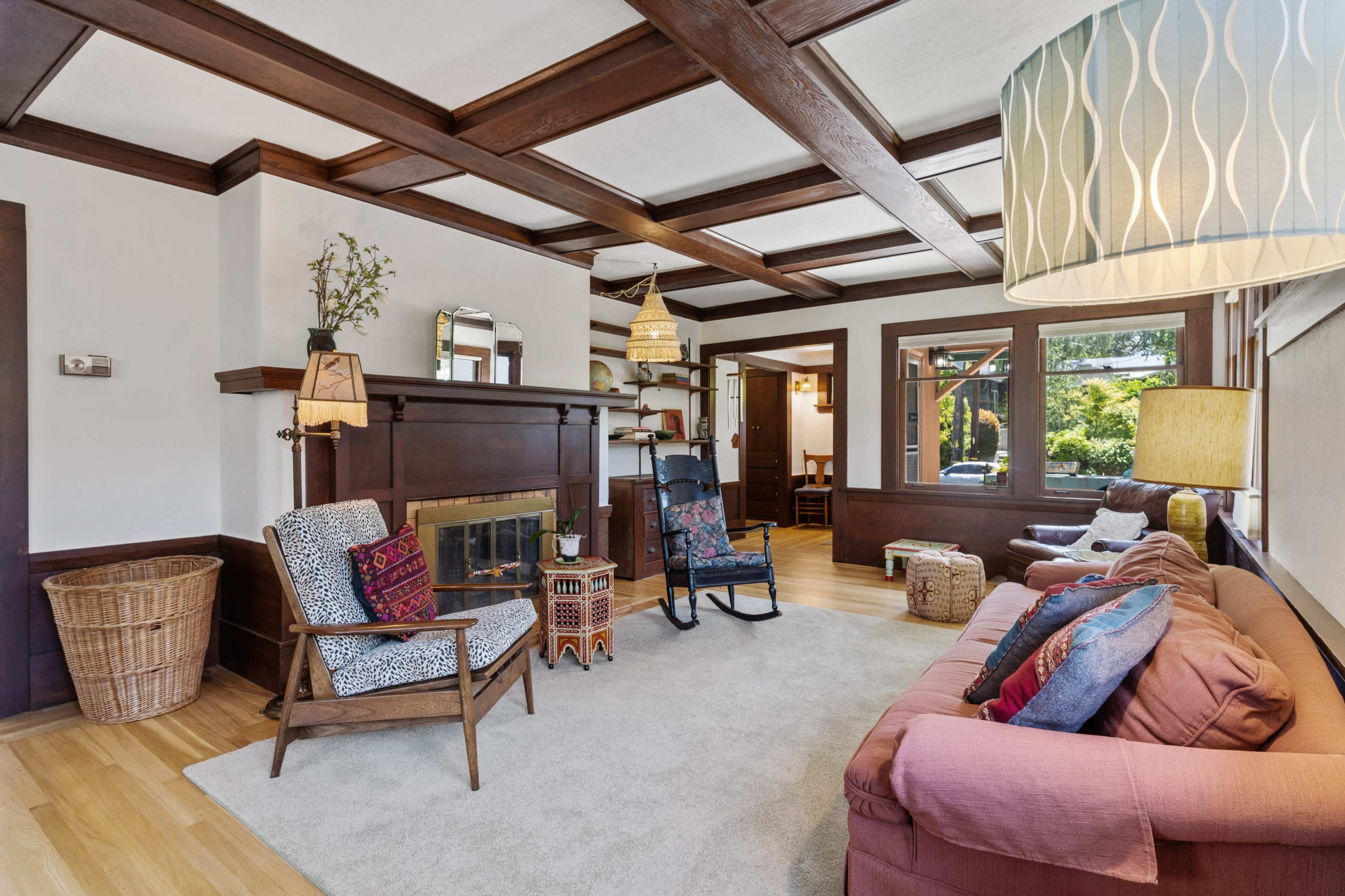 The living room features a combination of a couch, armchairs, and a fireplace, all accented by wood paneling and large windows.
