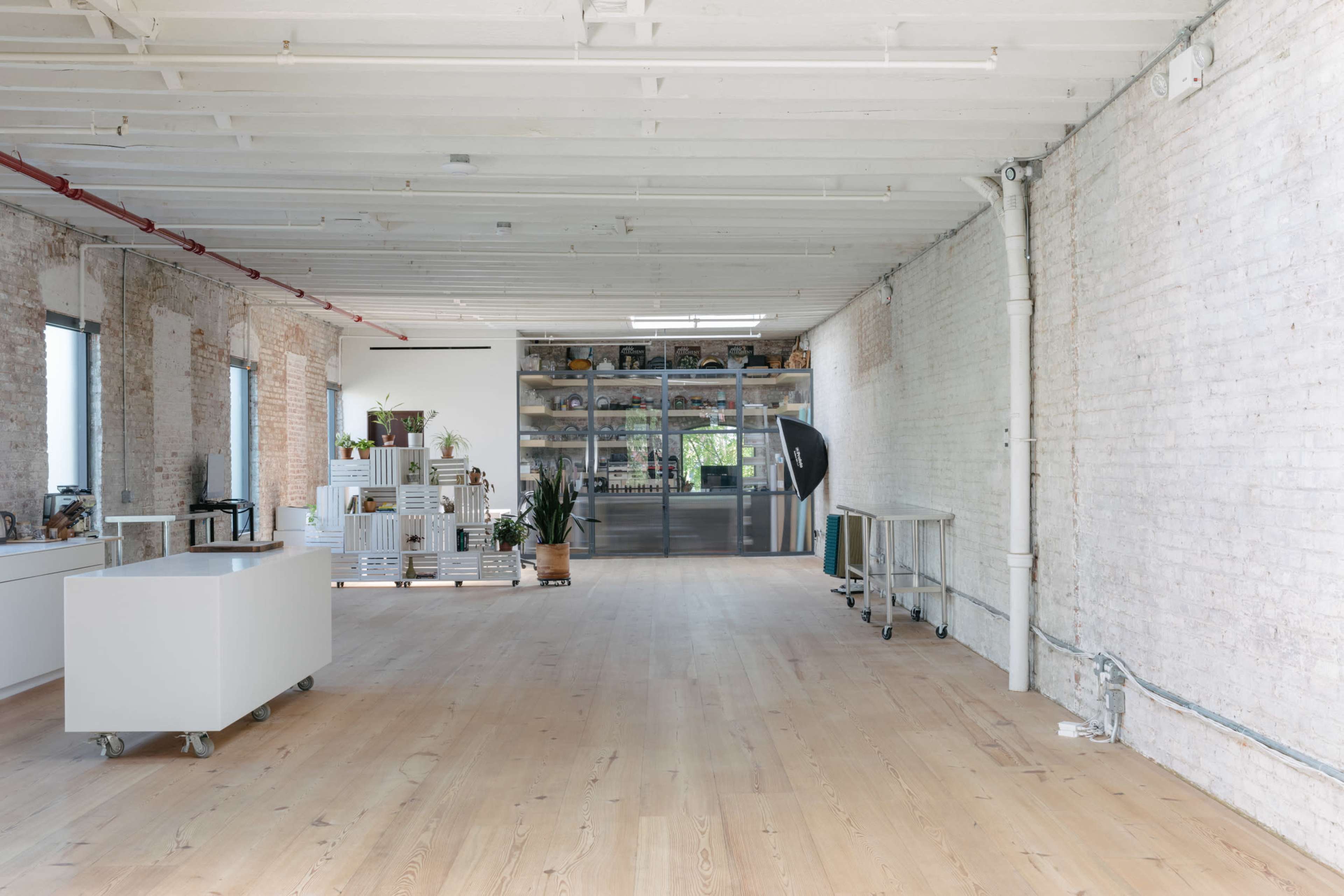 A spacious, well-lit room with wooden floors, white brick walls, and a large glass display cabinet against one wall.