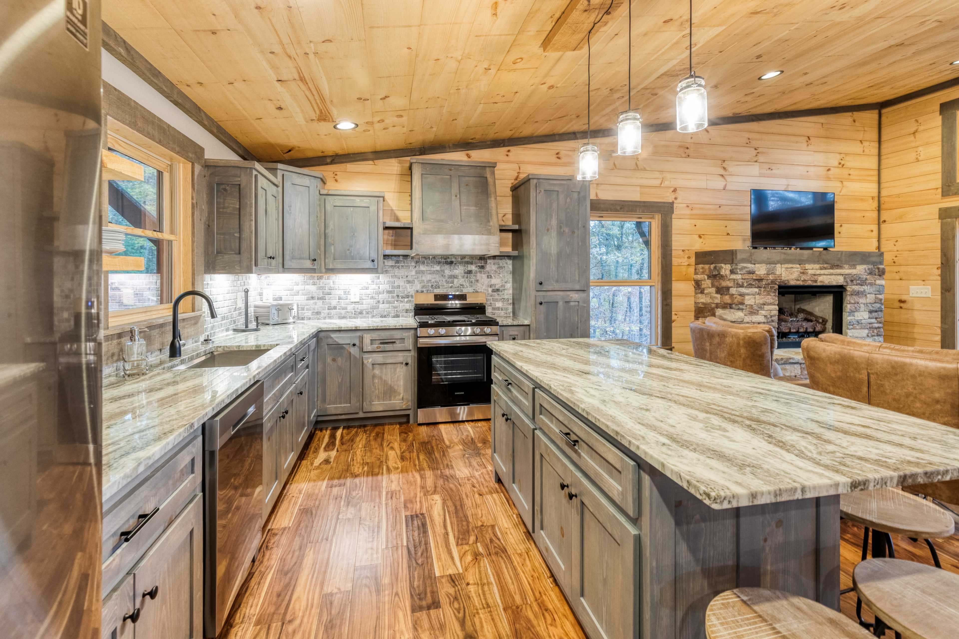 A modern kitchen with wooden cabinets, a large granite island, and a stone fireplace in a cozy setting.
