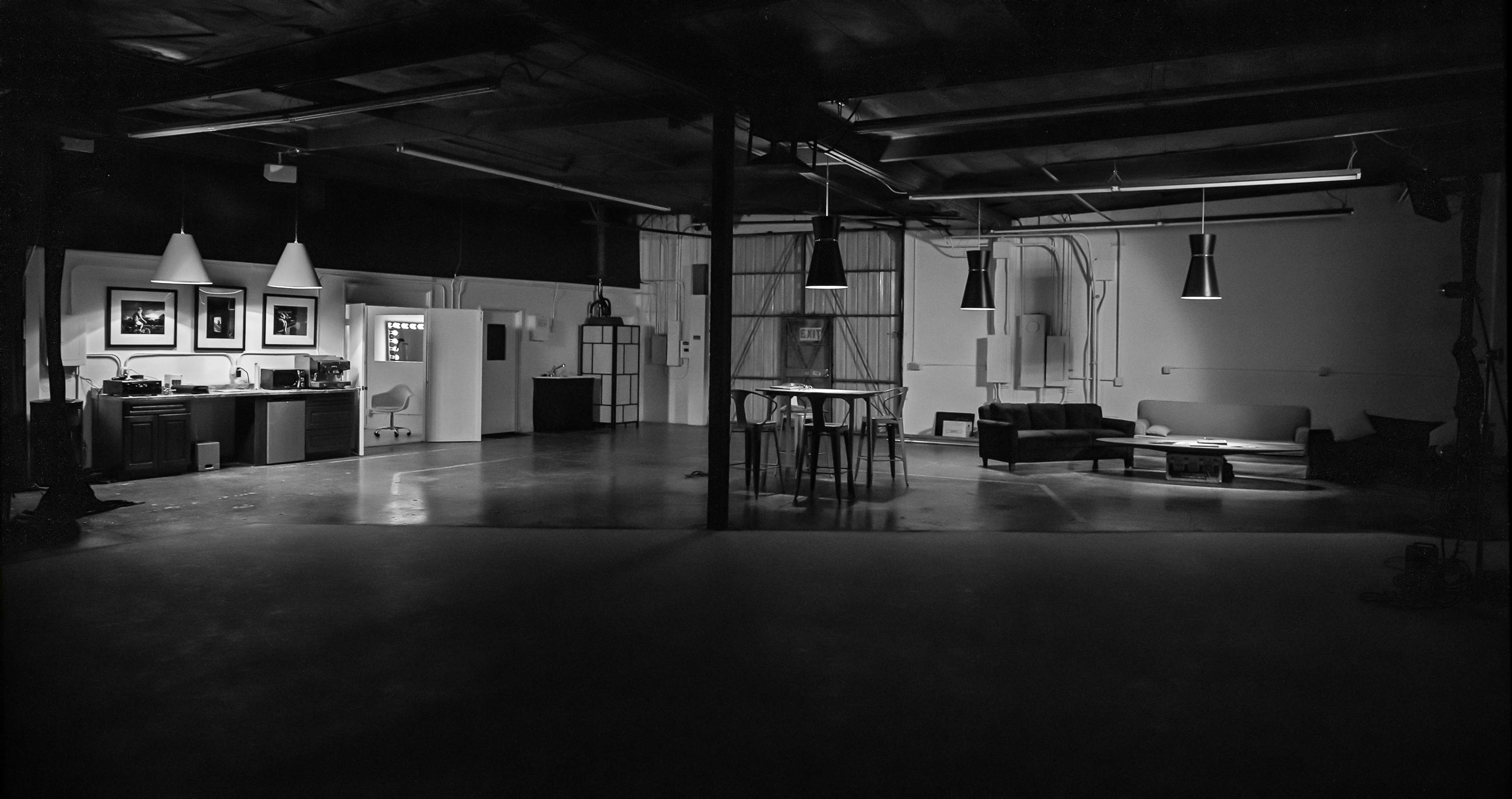 A spacious interior with a kitchen area, a dining table with stools, and a seating area that includes a sofa, all under industrial lighting.