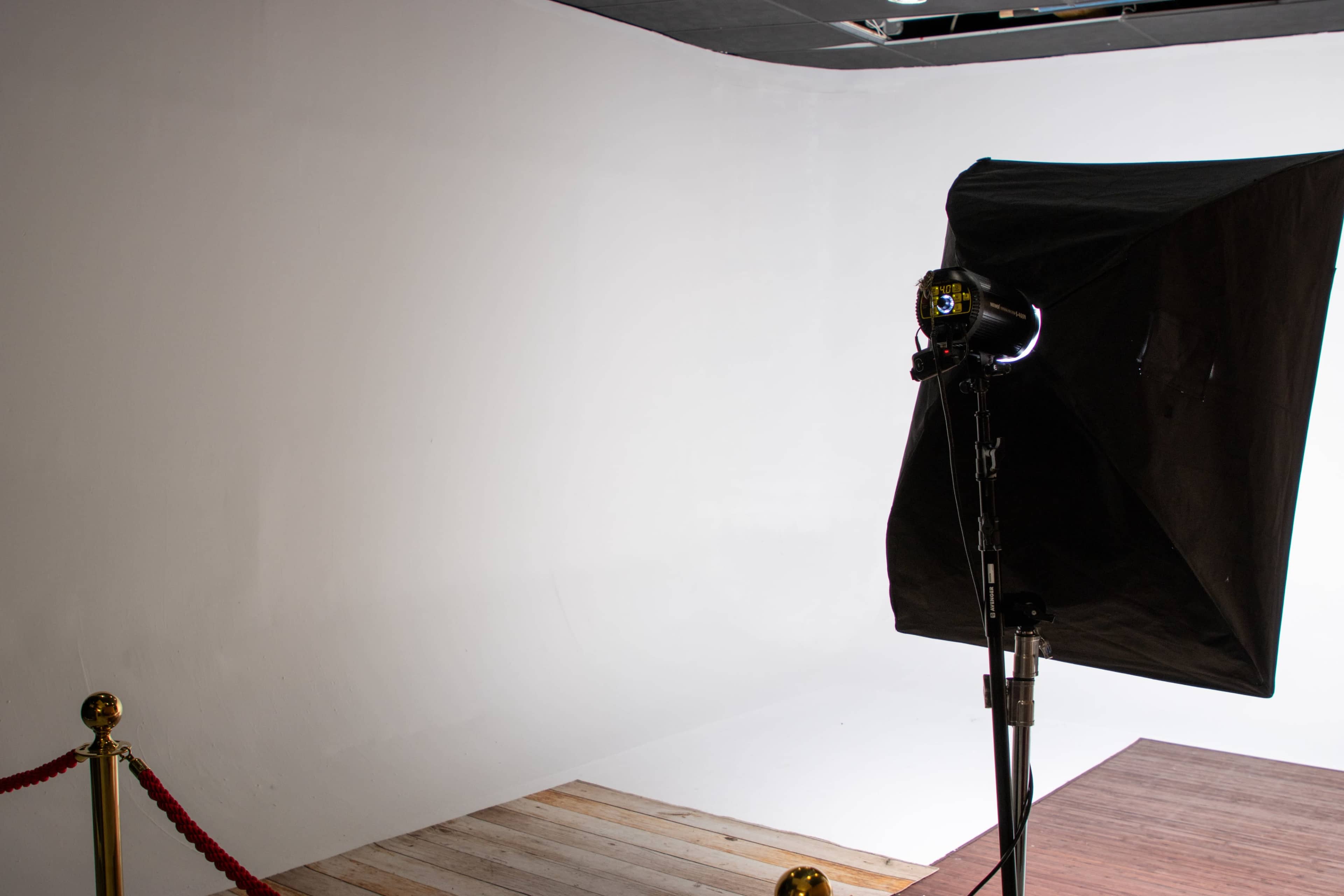 A photography studio setup with a black softbox light positioned beside a plain white backdrop.
