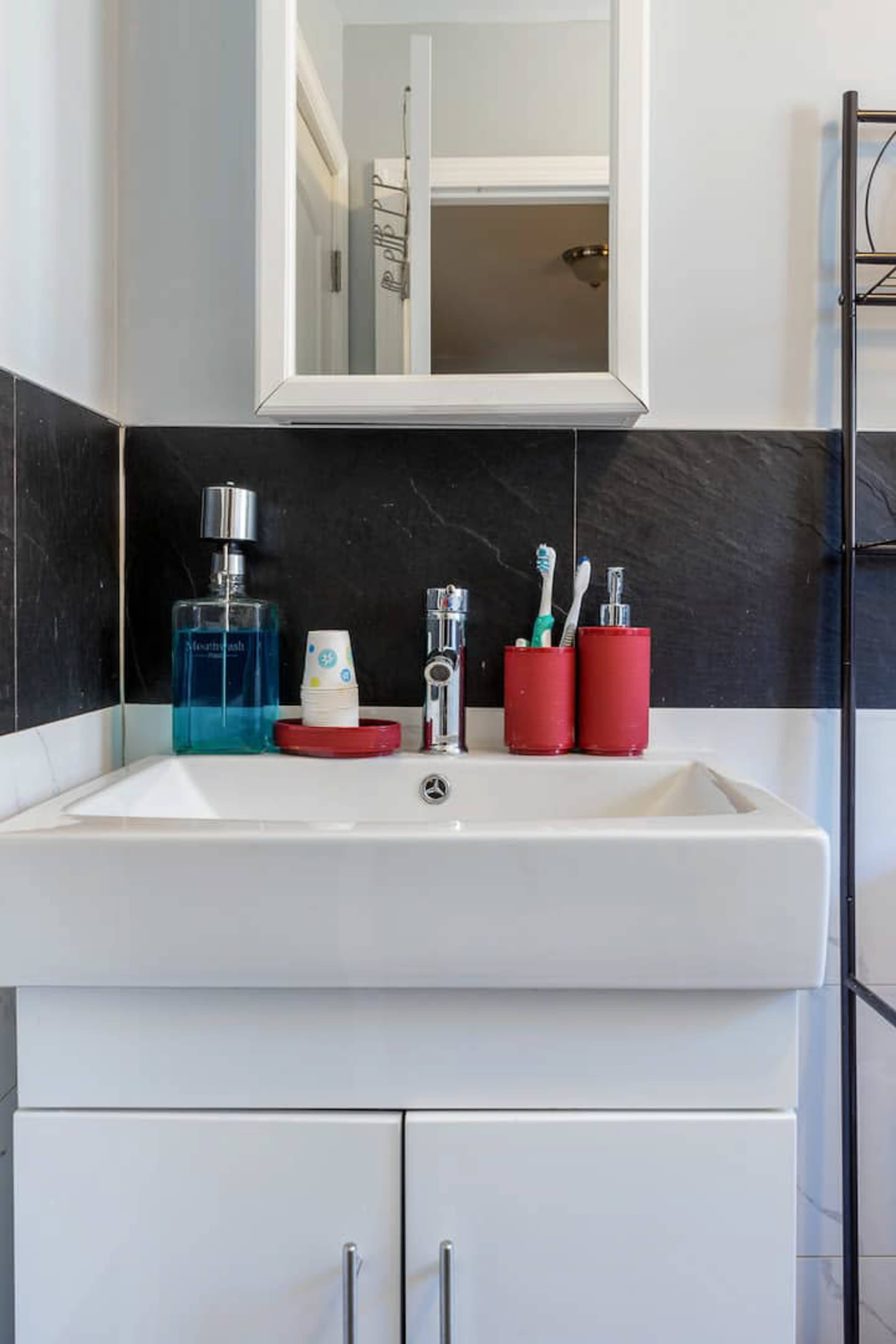 A bathroom sink with a white countertop, a mirror above it, and various toiletries neatly arranged nearby.