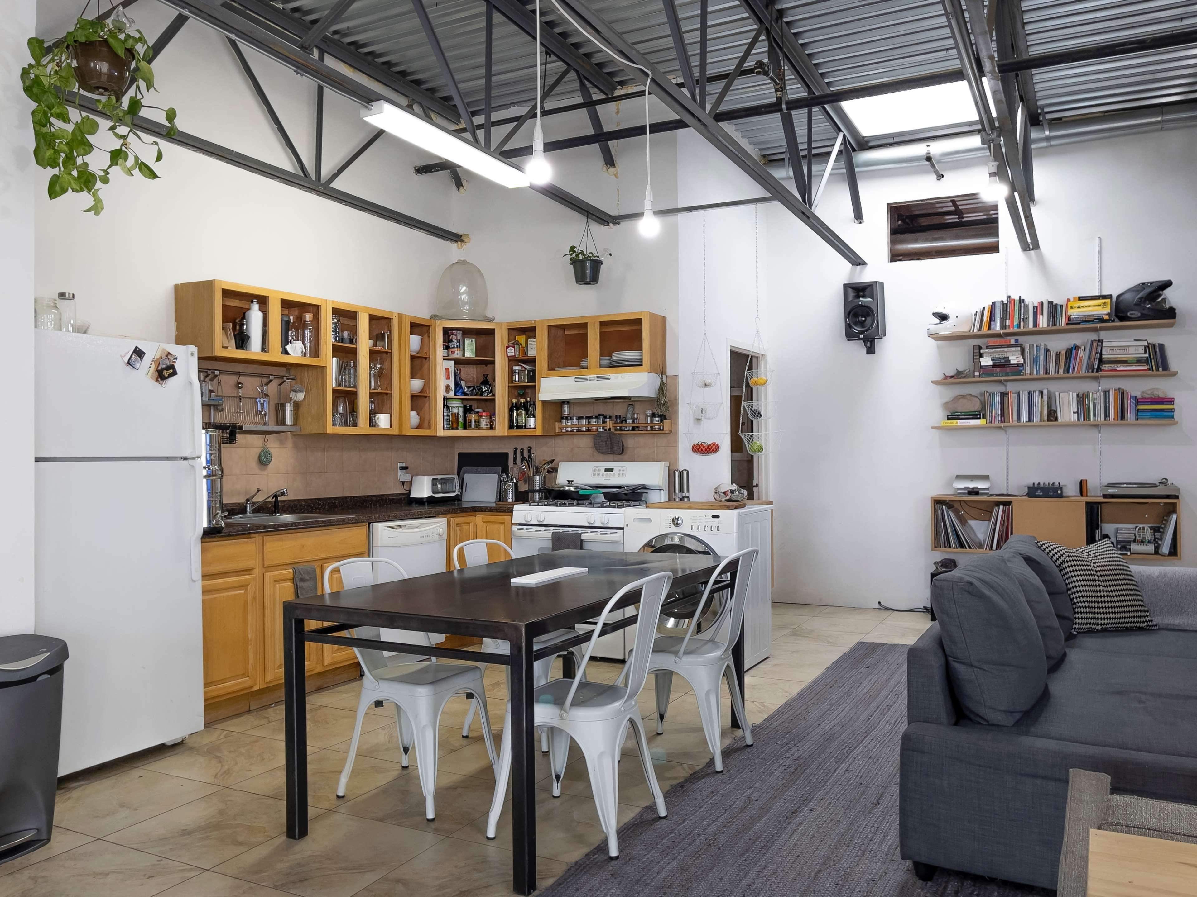 A spacious kitchen and dining area features a wooden table with metal chairs, a well-organized kitchen with cabinets, and a comfortable seating area with a couch.