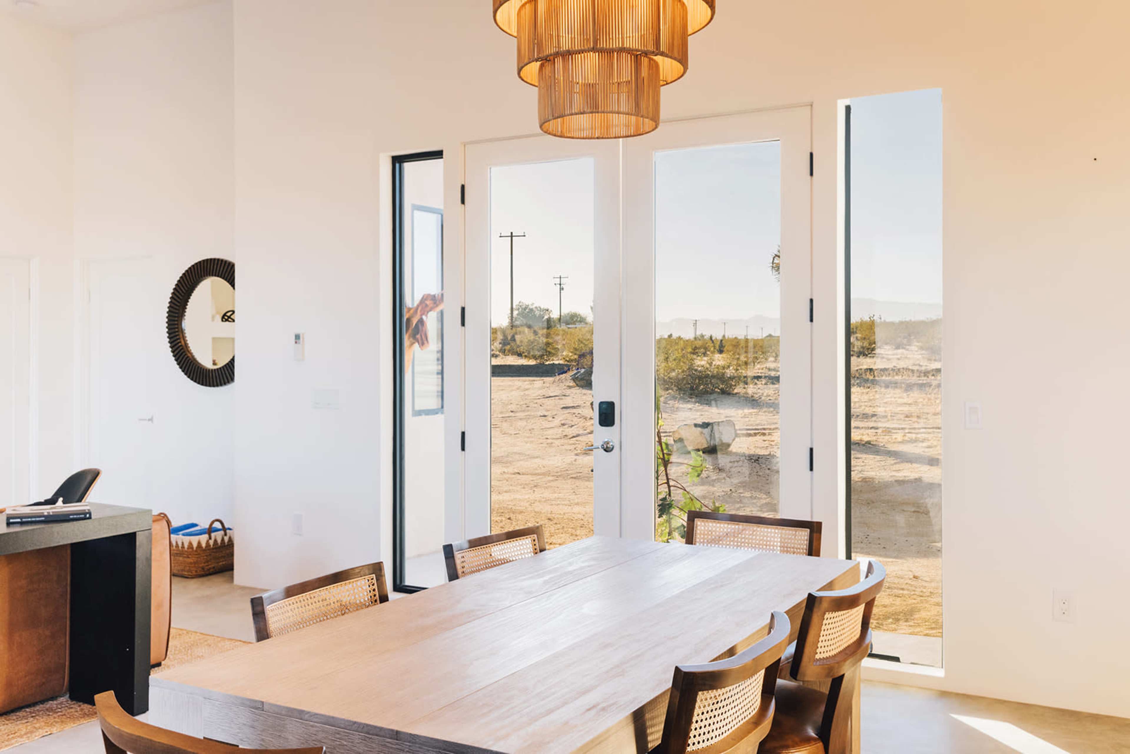 A modern dining area featuring a wooden table with eight chairs, large glass doors leading to an outdoor view, and a pendant light hanging above the table.