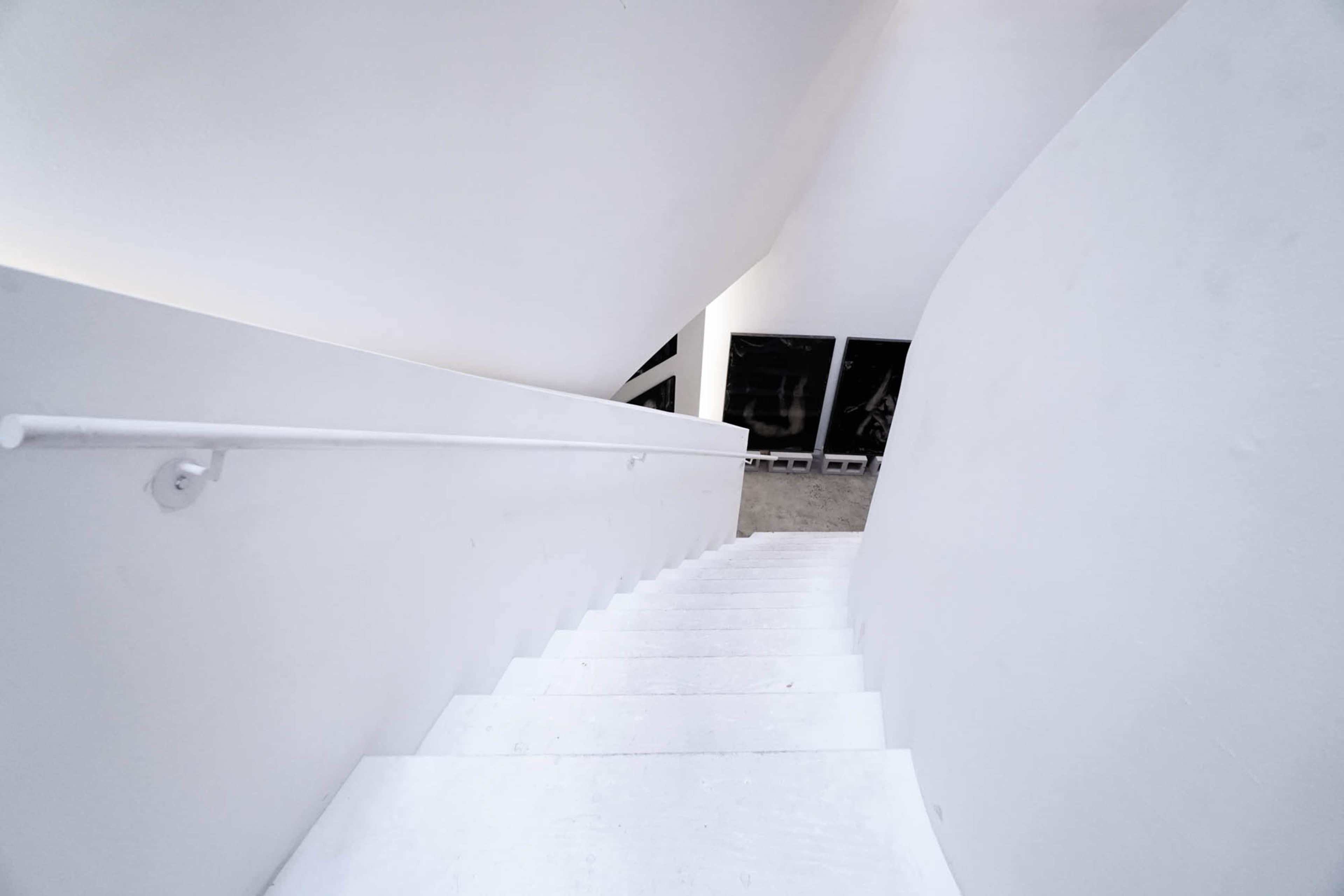 A white staircase curves downward to a lower level, with a smooth handrail on the right side.