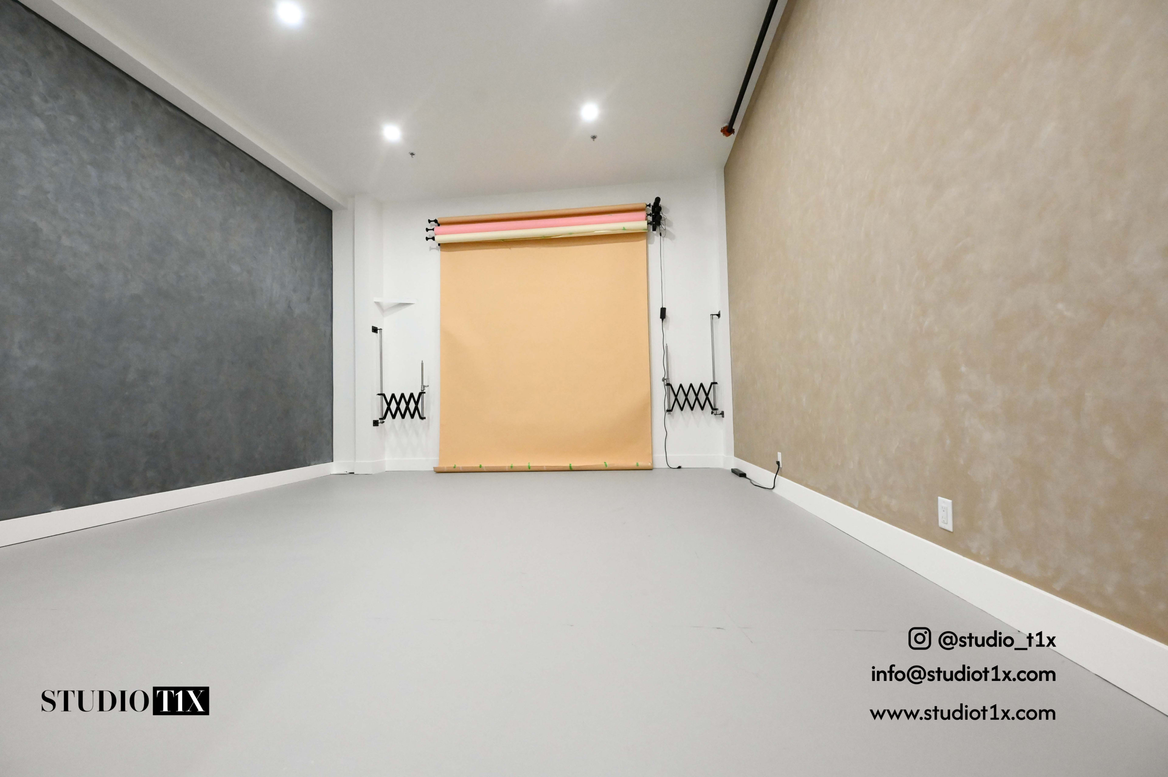 A spacious photography studio features a plain gray wall, a neutral backdrop setup, and a smooth floor.