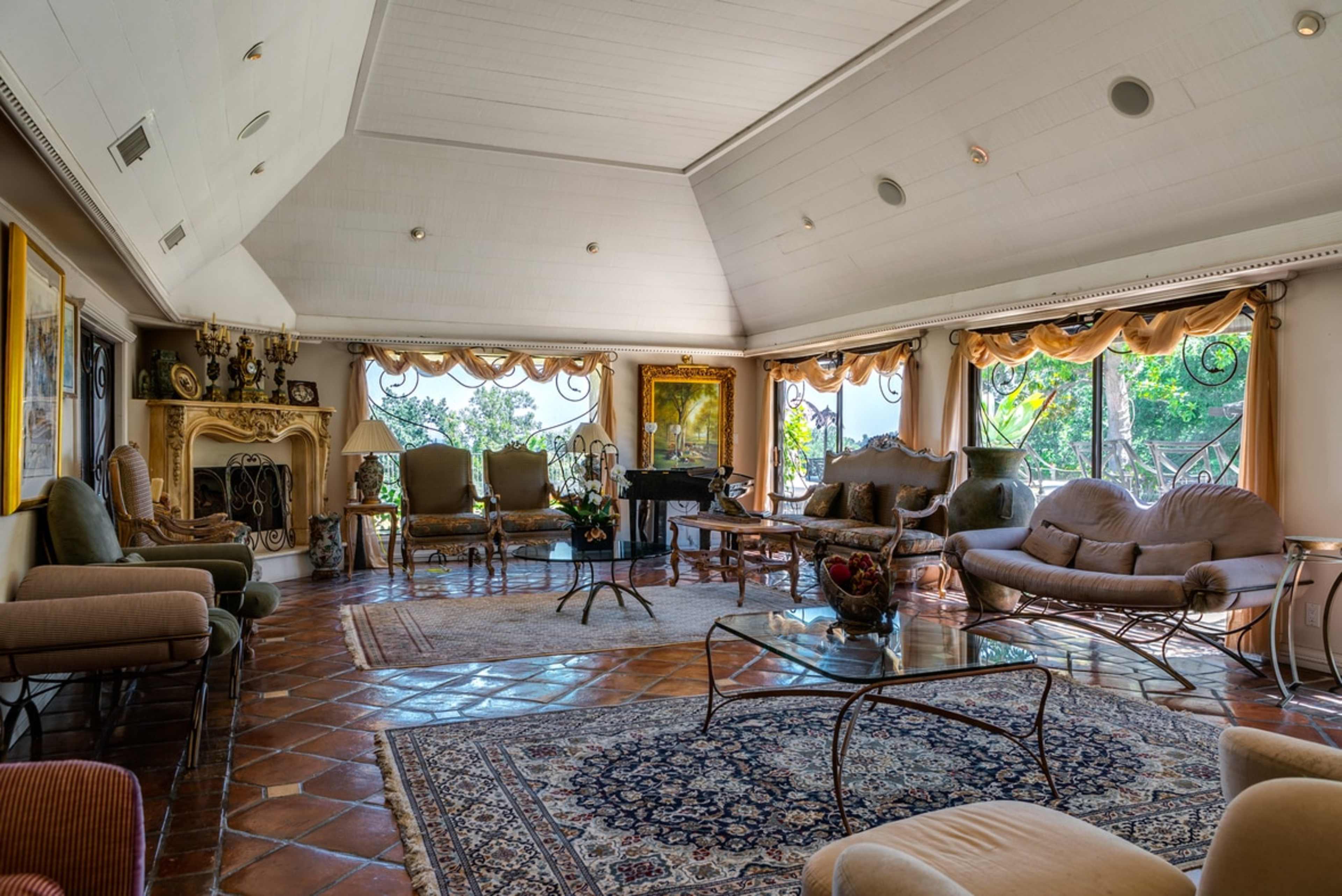 A spacious living room with large windows, a decorative fireplace, and a mix of elegant furniture arranged around a glass coffee table.