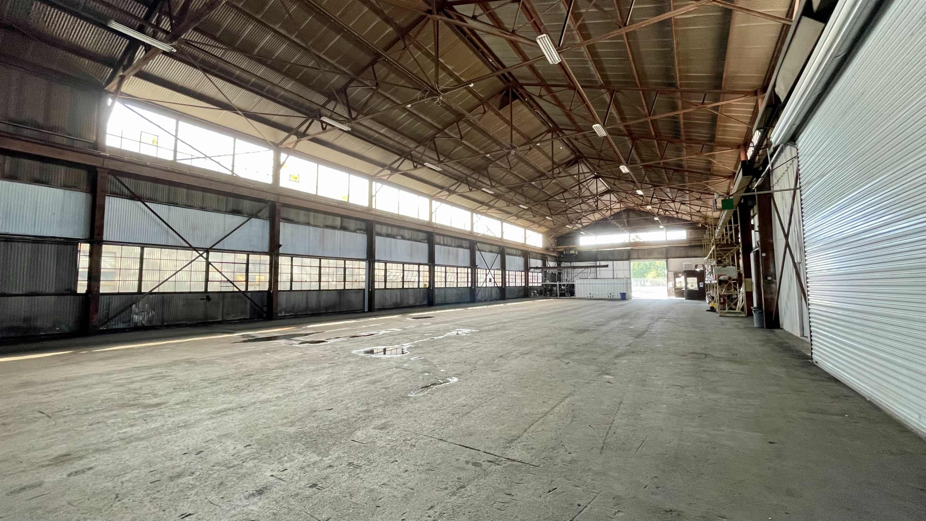 A spacious, industrial warehouse with high ceilings, large windows, and a concrete floor.