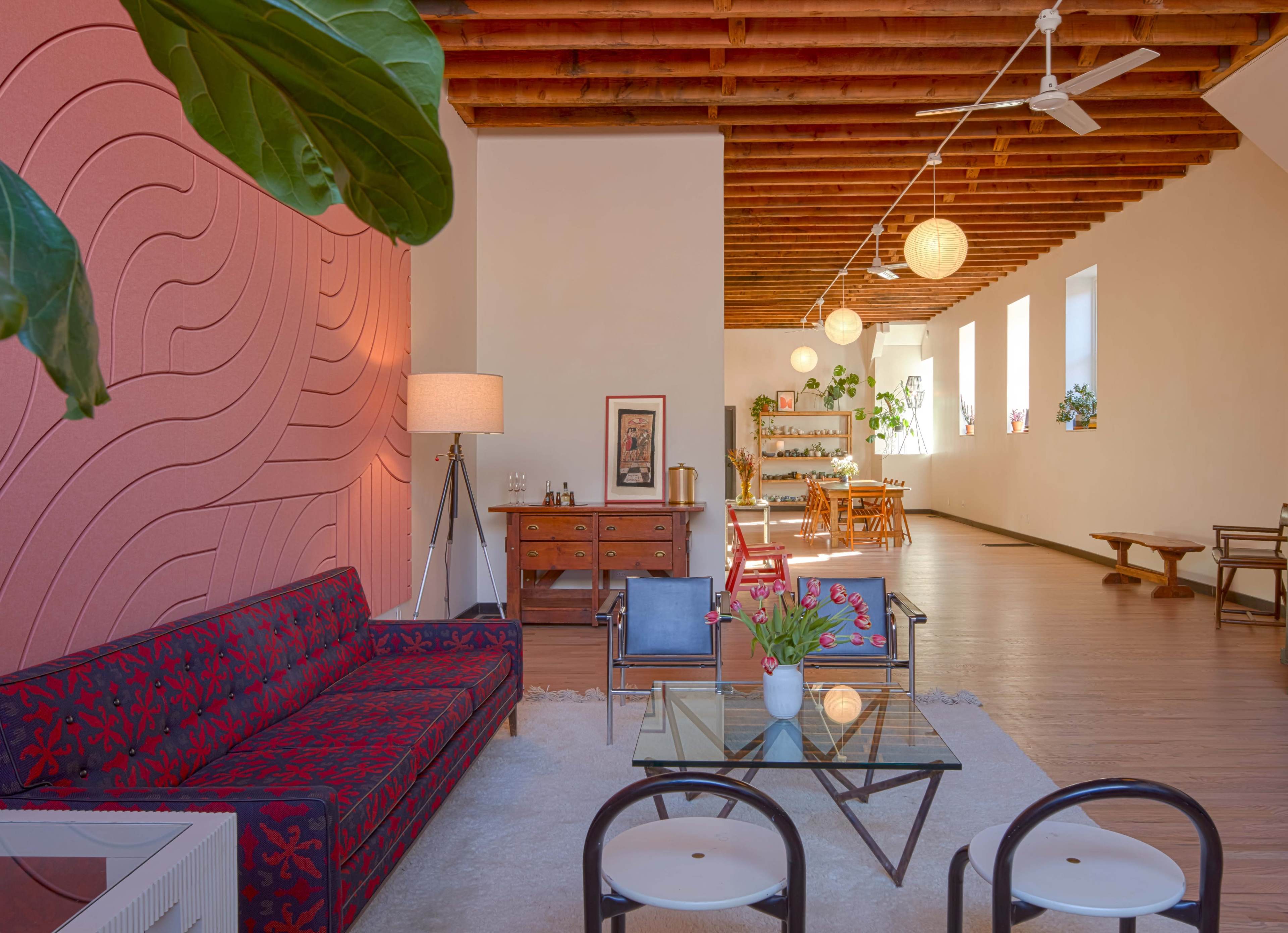 A modern living space features a patterned sofa, a glass coffee table, and a dining area with wooden furniture under wooden beams and ambient lighting.
