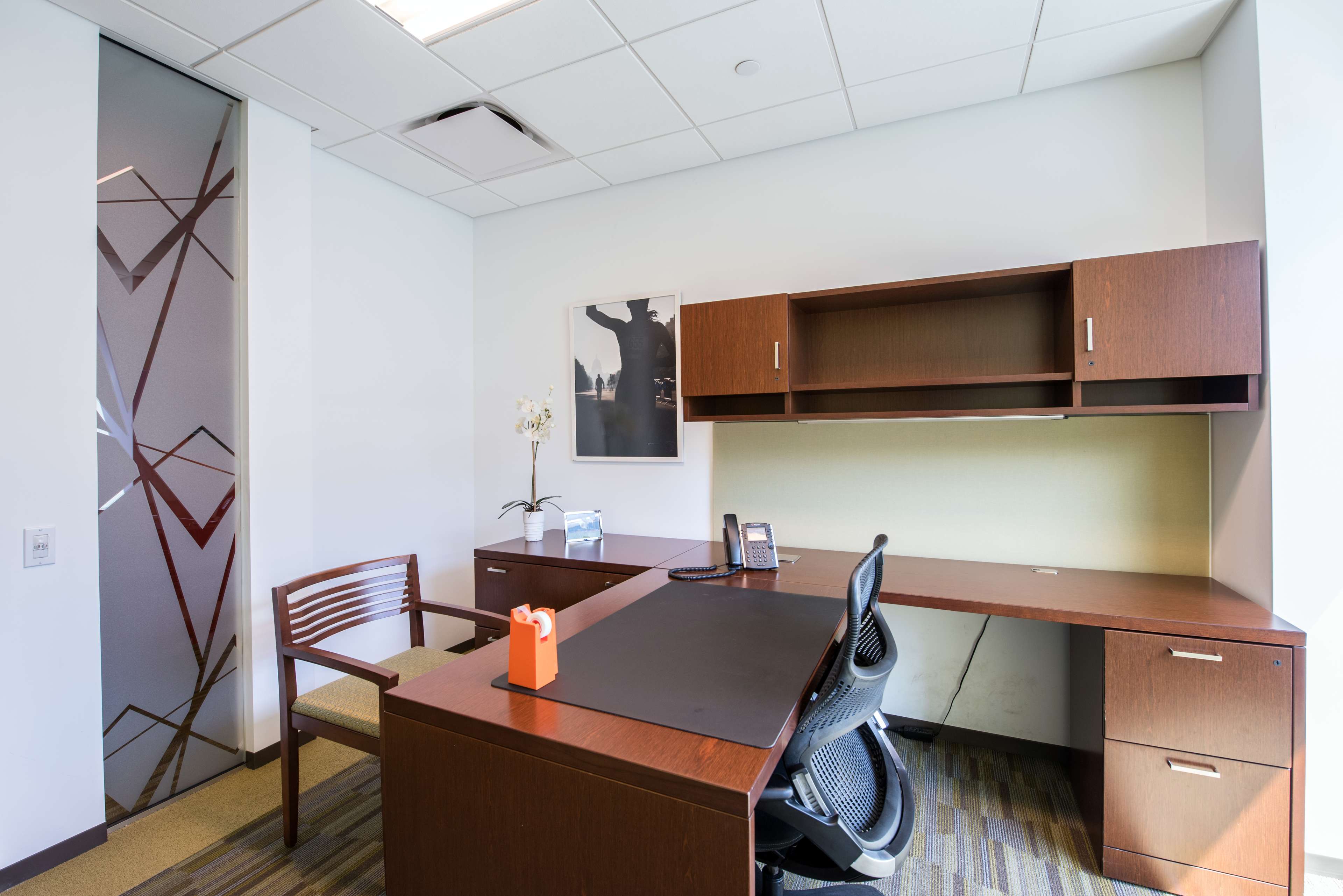 The image shows a modern office space with a wooden desk, an ergonomic chair, and a decorative partition in the background.