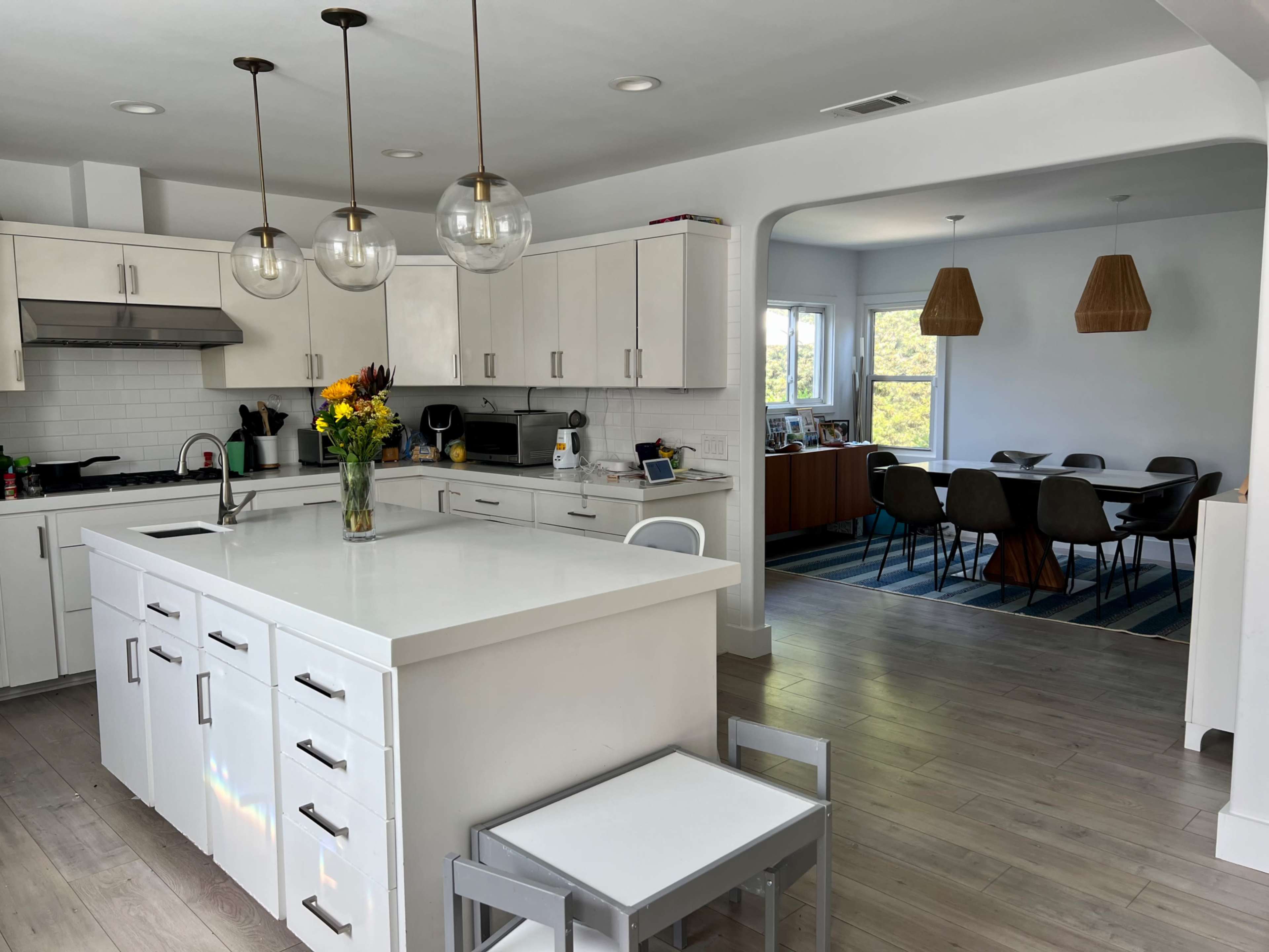 A modern kitchen features white cabinetry, a large island with a sink, and a dining area visible through an archway.