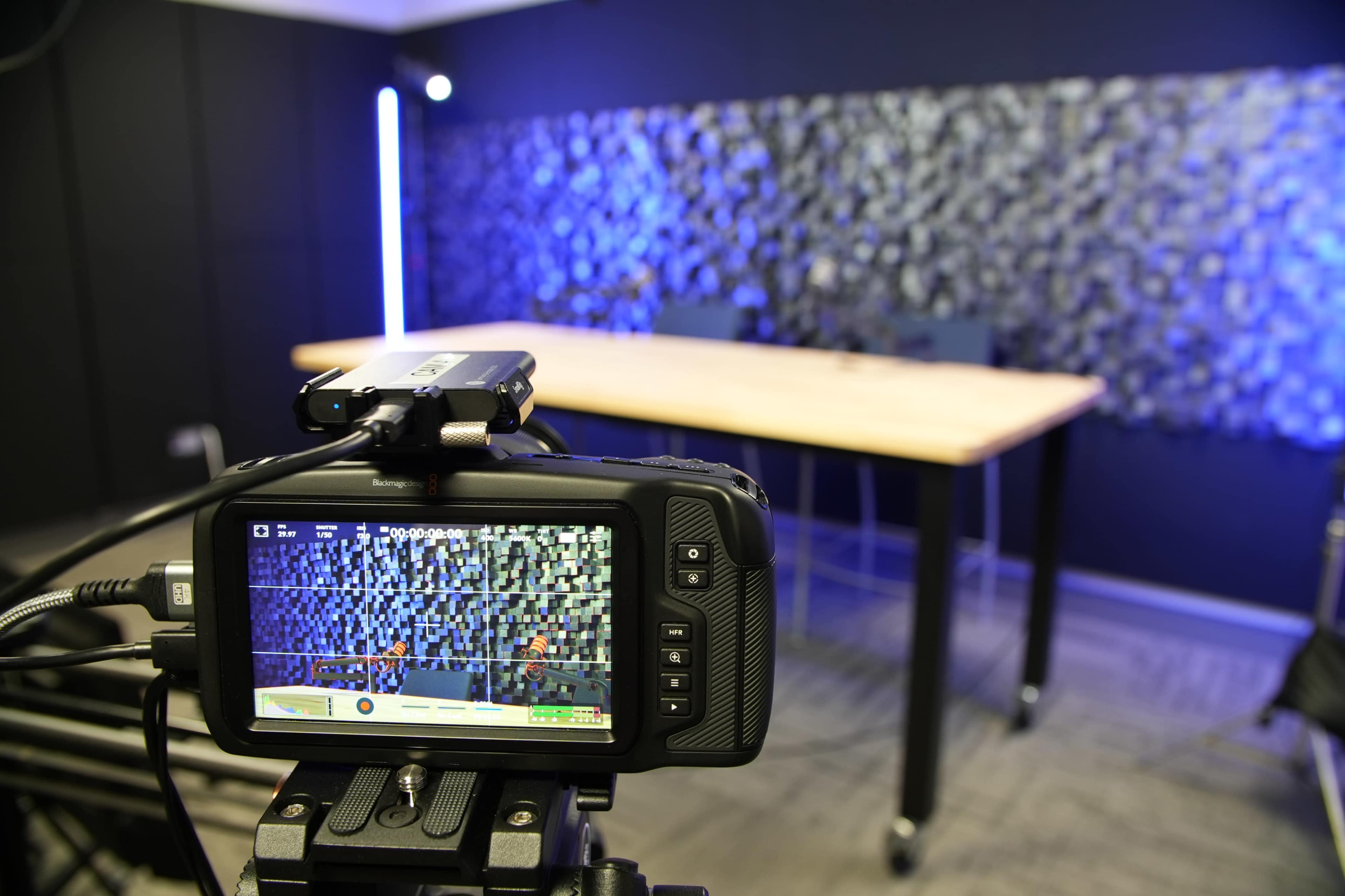 A camera is positioned in front of a wooden table set against a textured blue and gray wall, ready for recording.