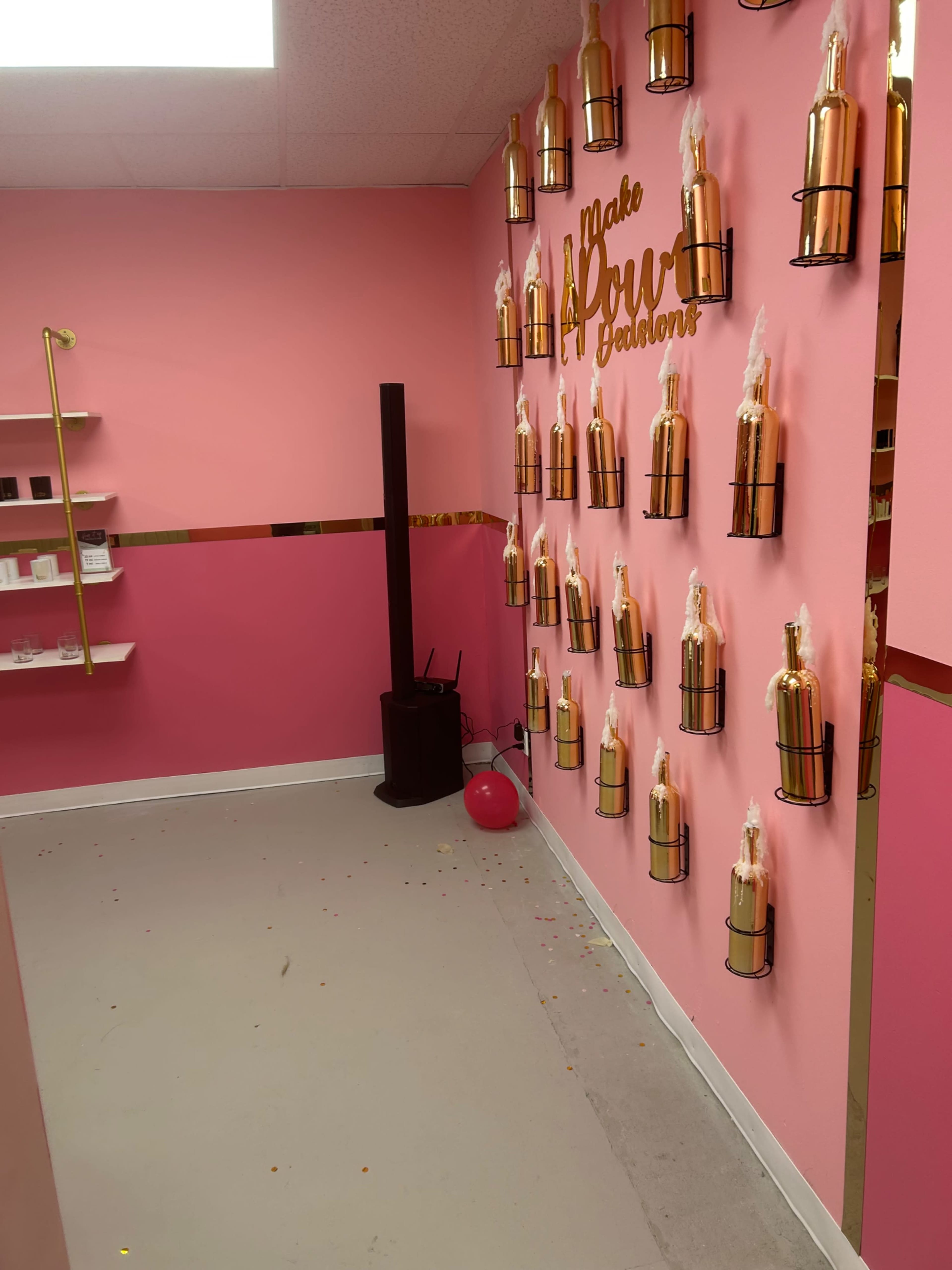 The image shows a pink-walled room with decorative bottles mounted on the wall, a shelf on the left, and scattered confetti on the floor.
