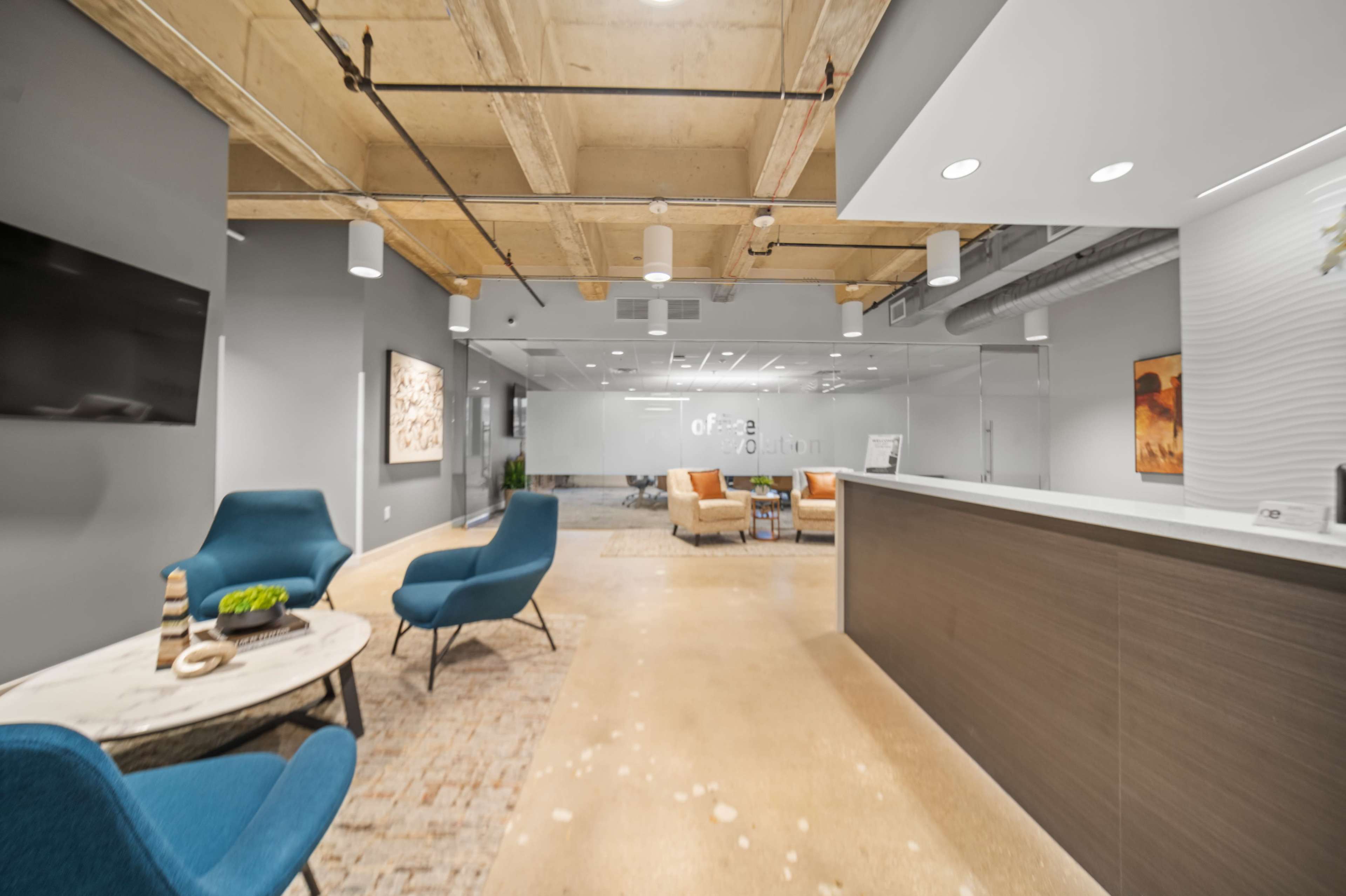 The image shows a modern office reception area with a front desk, seating options, and large windows separating it from the adjacent workspace.