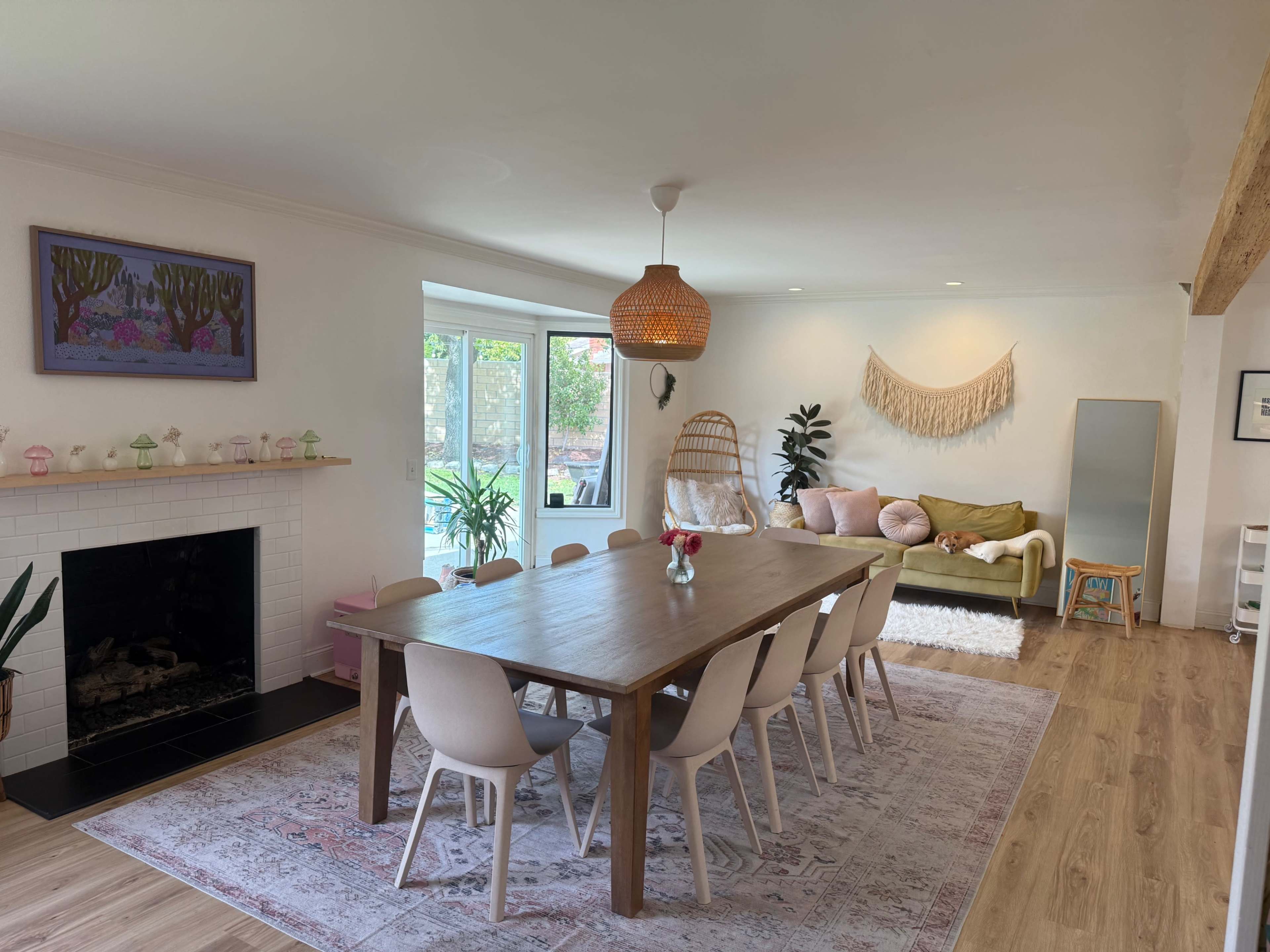 A spacious dining area features a long wooden table surrounded by light-colored chairs, with a cozy seating area and large windows that provide ample natural light.