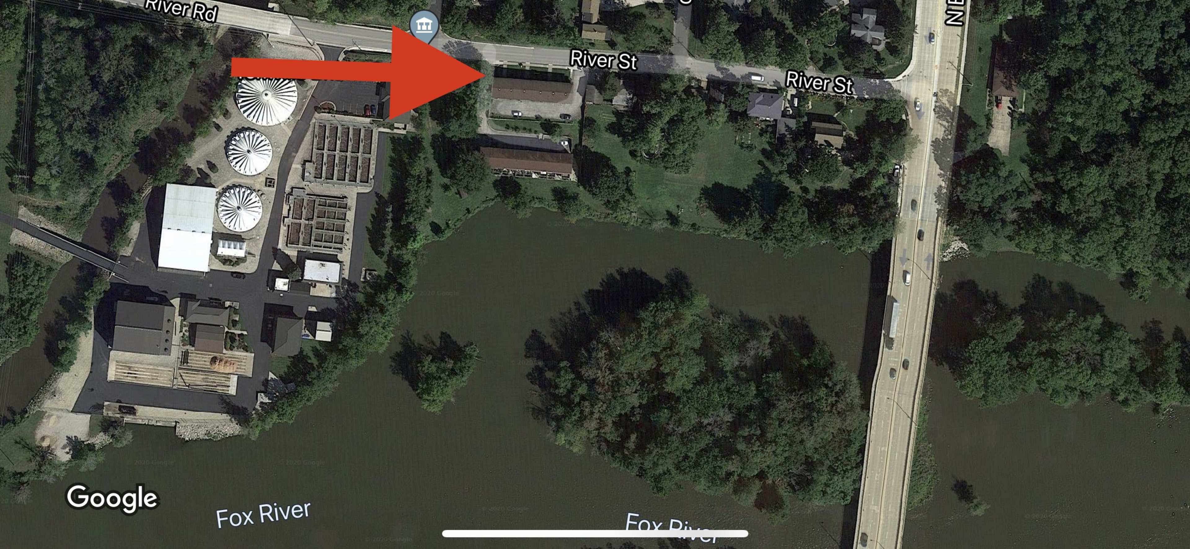 An aerial view of a portion of a river with nearby buildings, roads, and silos along the bank.