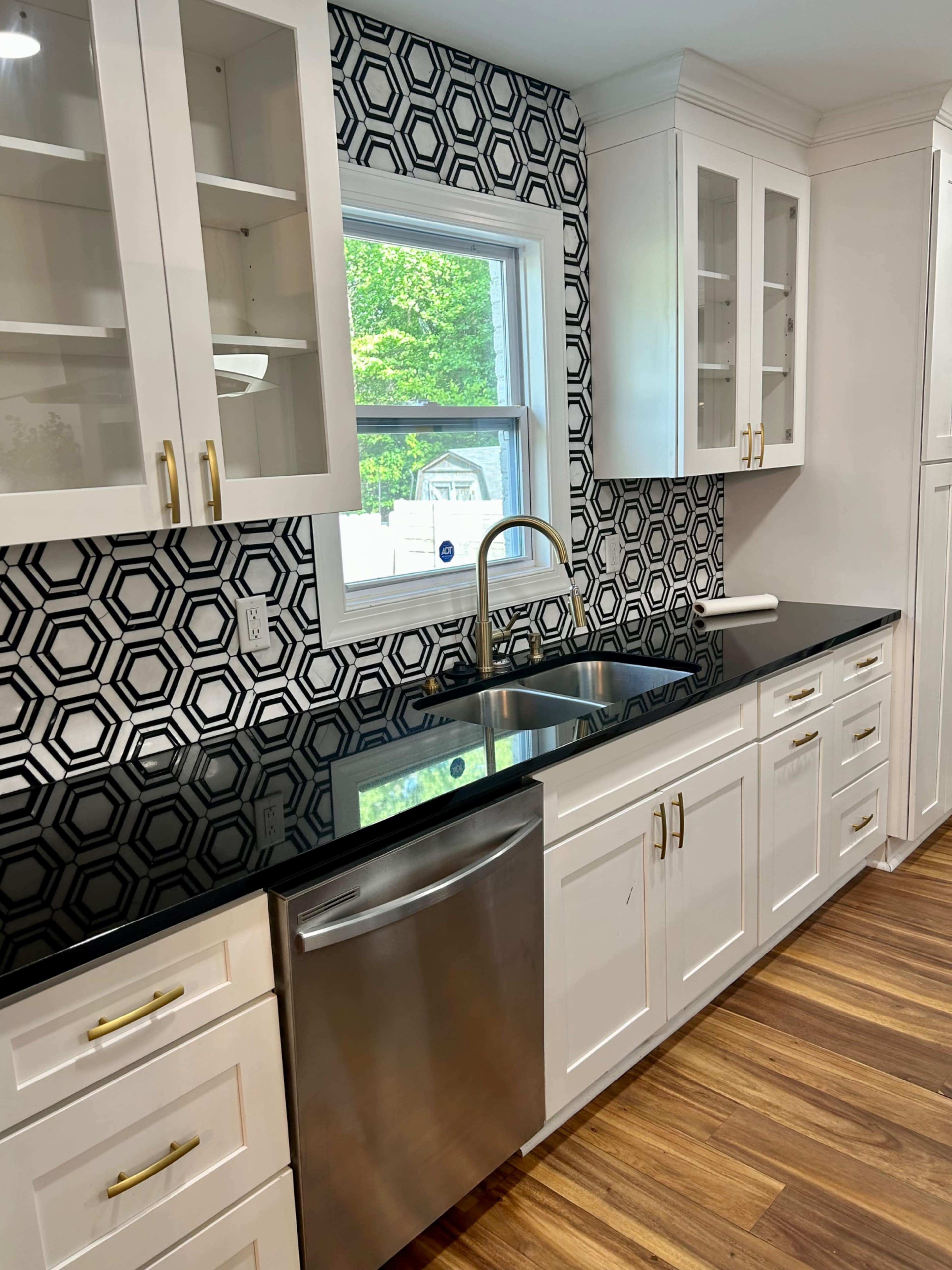 A modern kitchen features white cabinetry, a black countertop, and a geometric patterned backsplash.