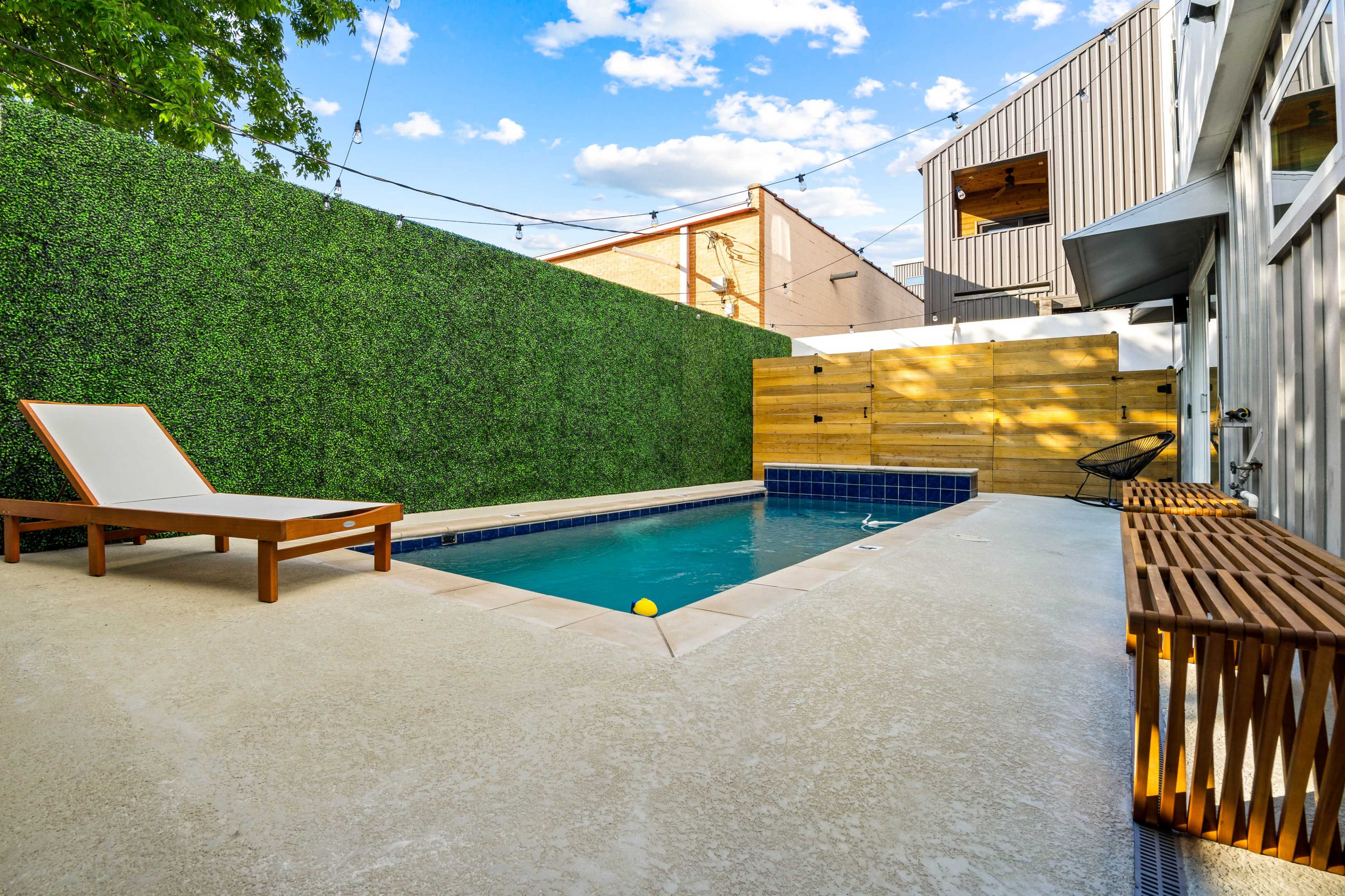 A backyard pool area with a lounge chair, surrounded by green walls and wooden fencing.