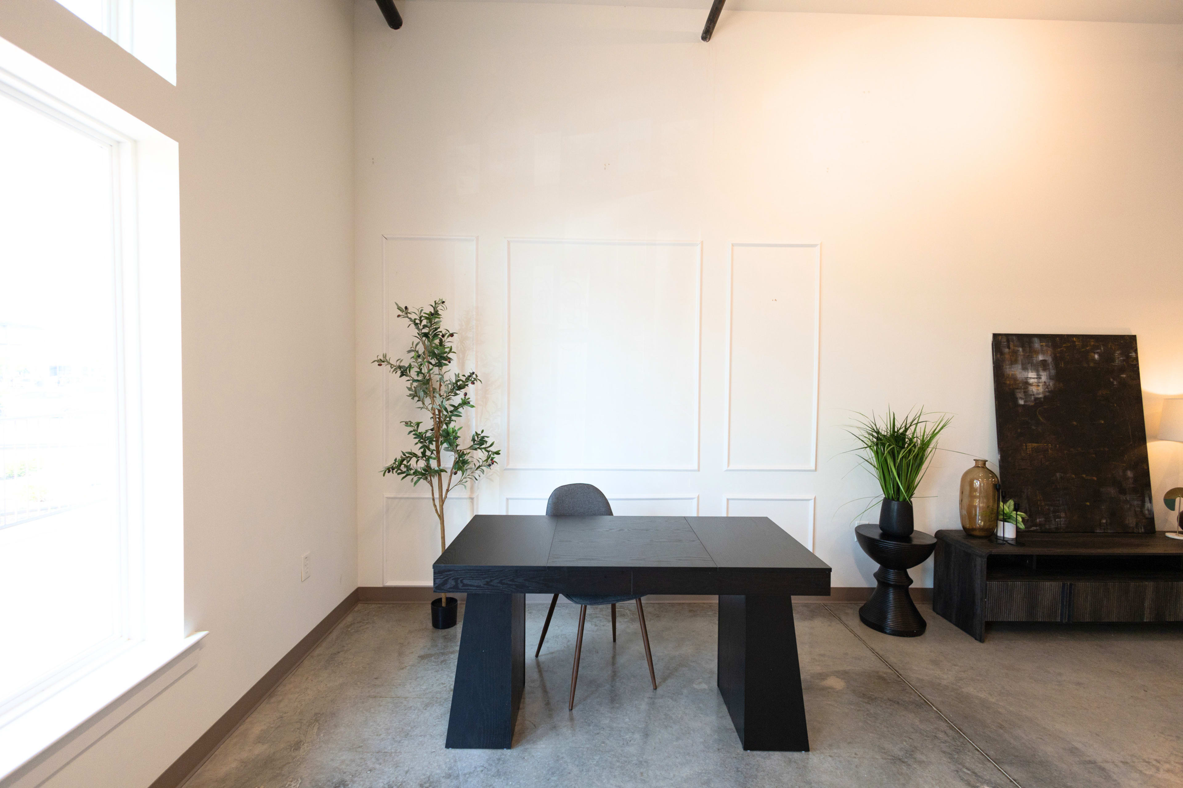 A modern interior features a black table with a single chair, accompanied by a plant and decorative items in a minimalistic setting.